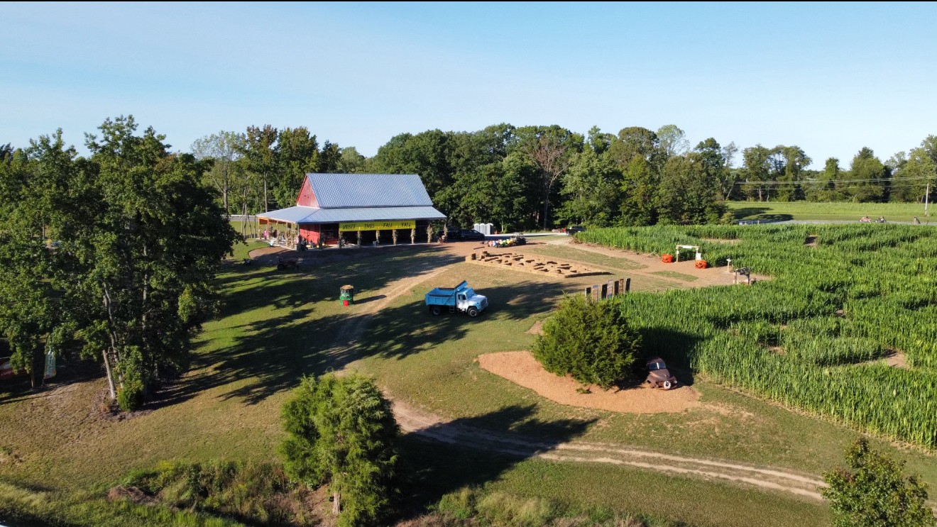 A rural farm scene with a barn, a parked car, and fields, under a clear blue sky.