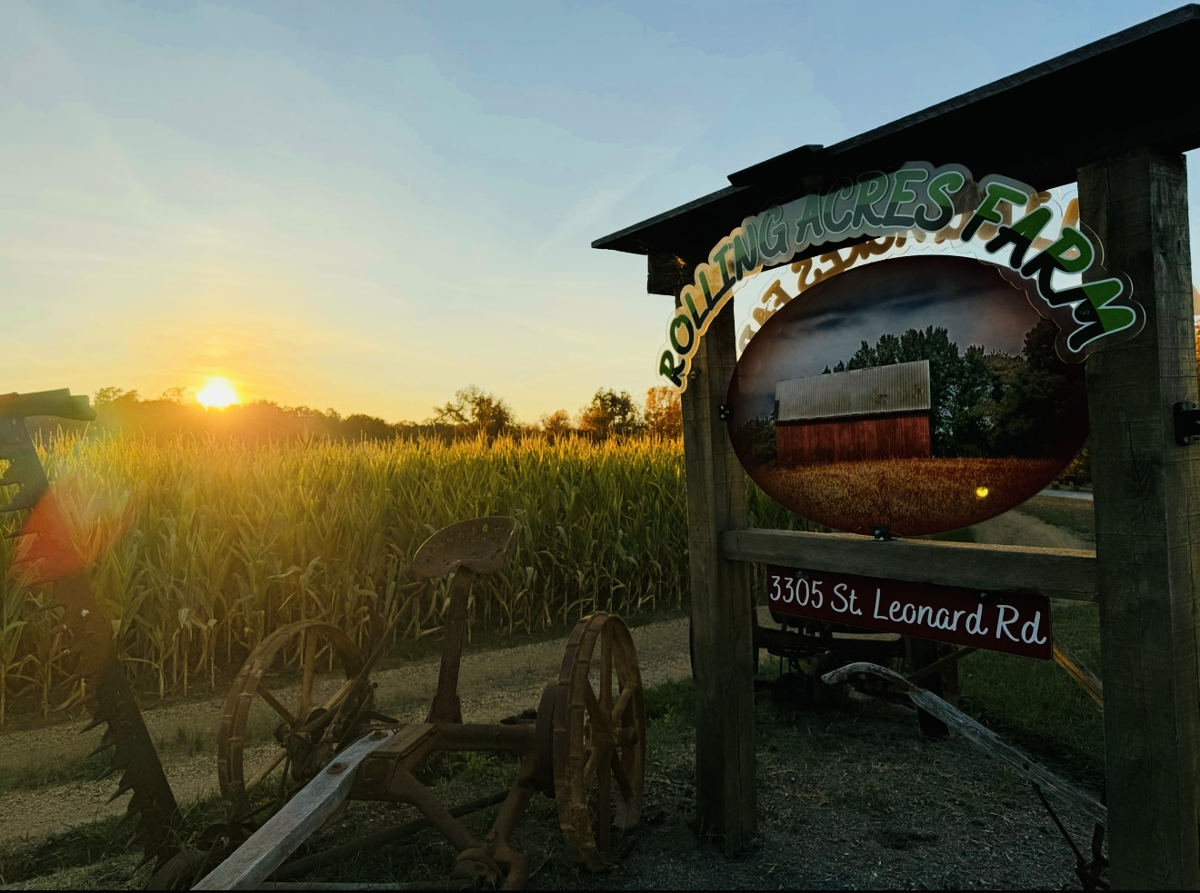 Sunset over a field with a wooden wagon and a sign for a farm, with a building reflected in a mirror.