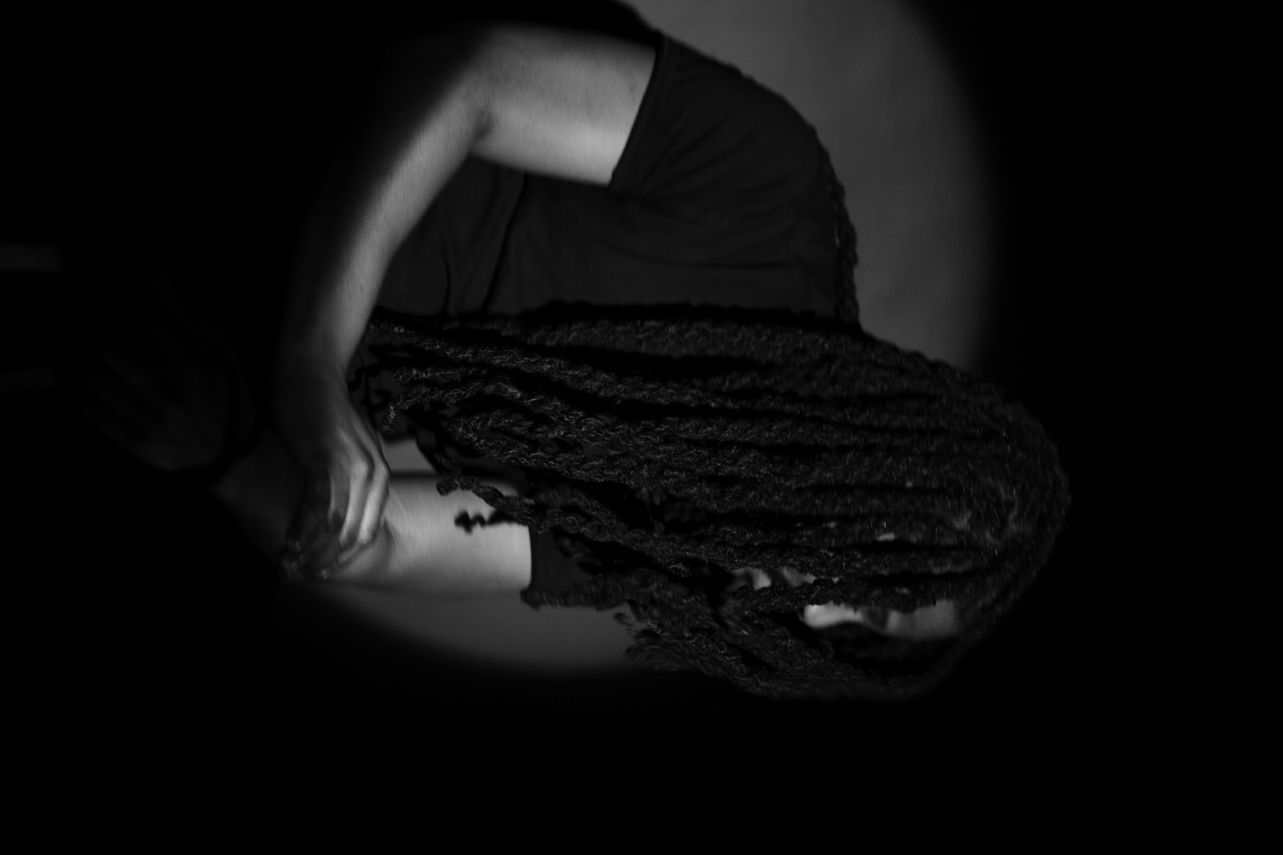 Person lying on side with head resting on arm, wearing dark clothing, in a dark setting.