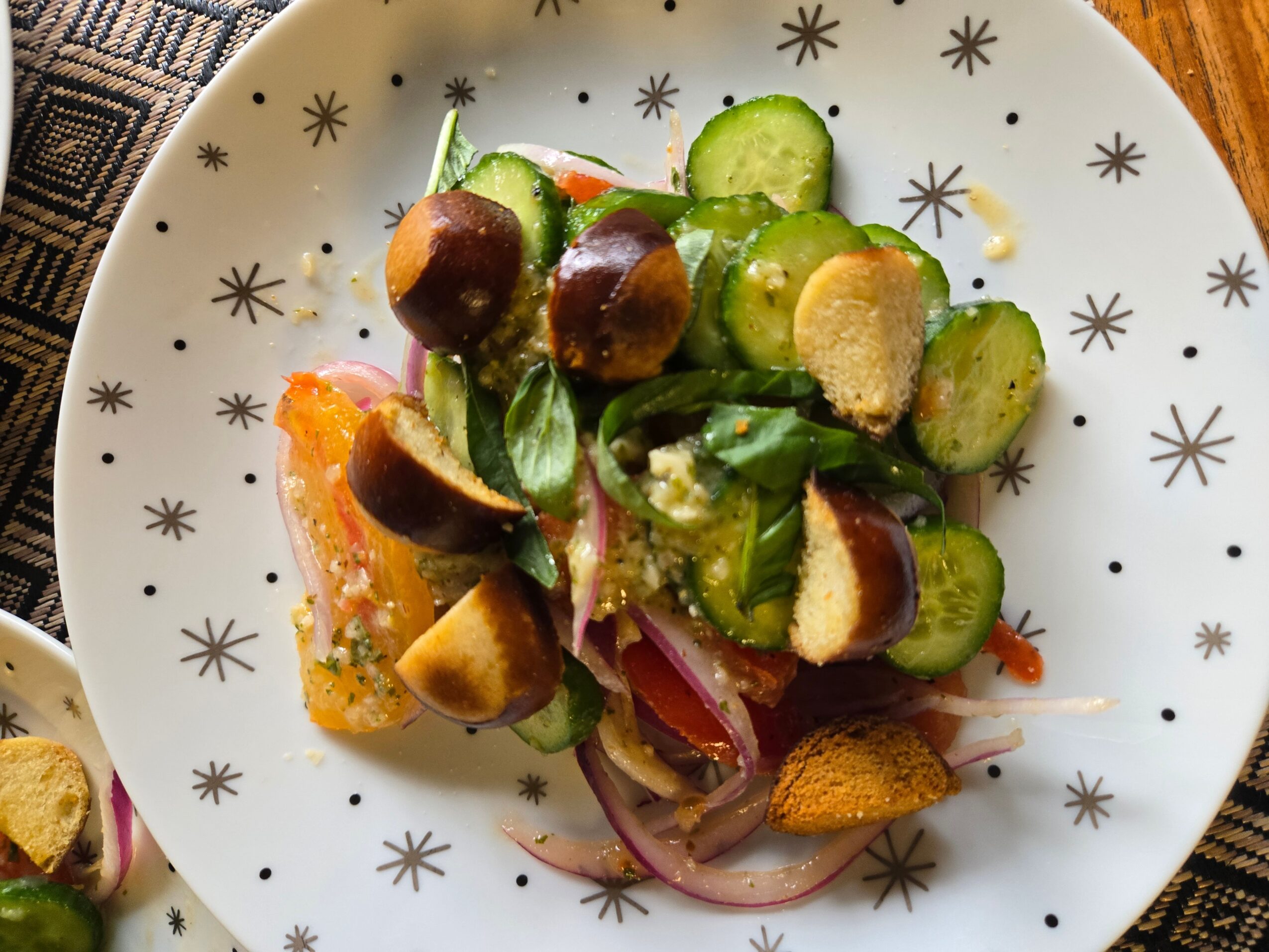 Cucumber, cherry tomato, and onion salad with herbs on a white plate with star patterns.