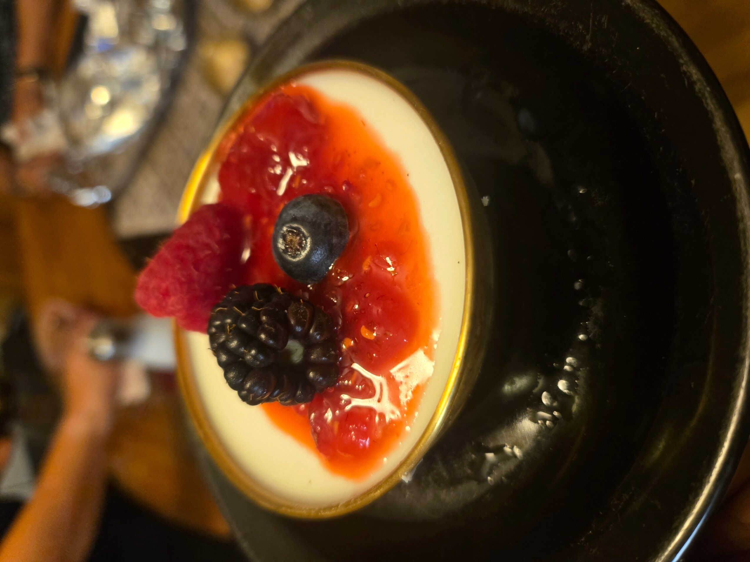 Dessert with berries and red sauce on a white base, in a black dish.