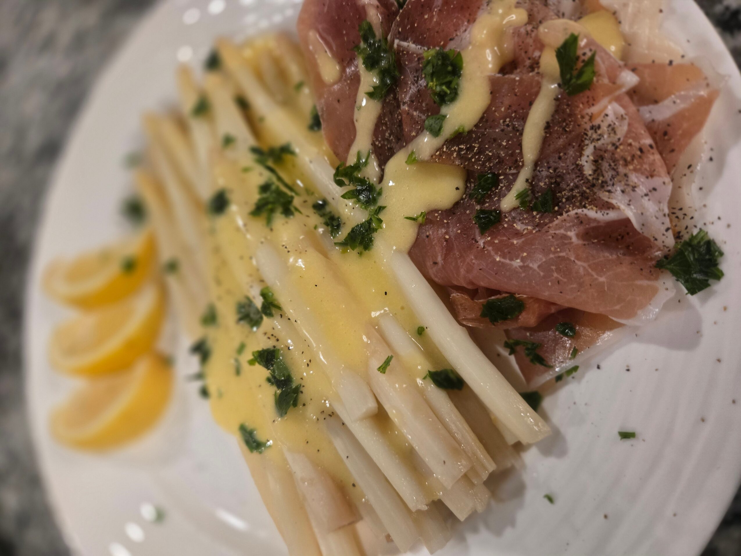 Plate with pasta, sliced lemon, prosciutto, and garnishes, viewed from above.