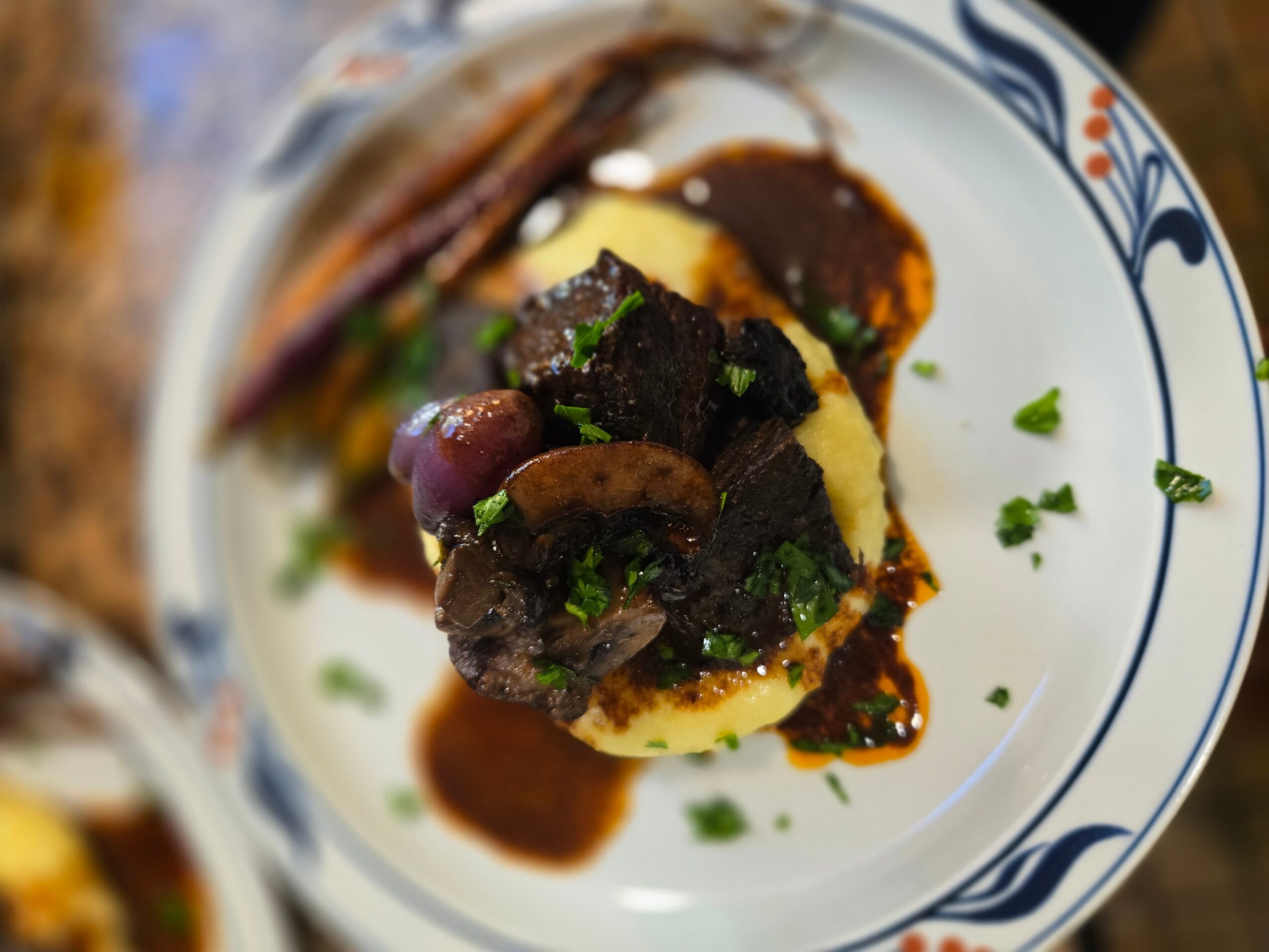Steak with mashed potatoes and sauce on a decorative plate, garnished with green herbs.