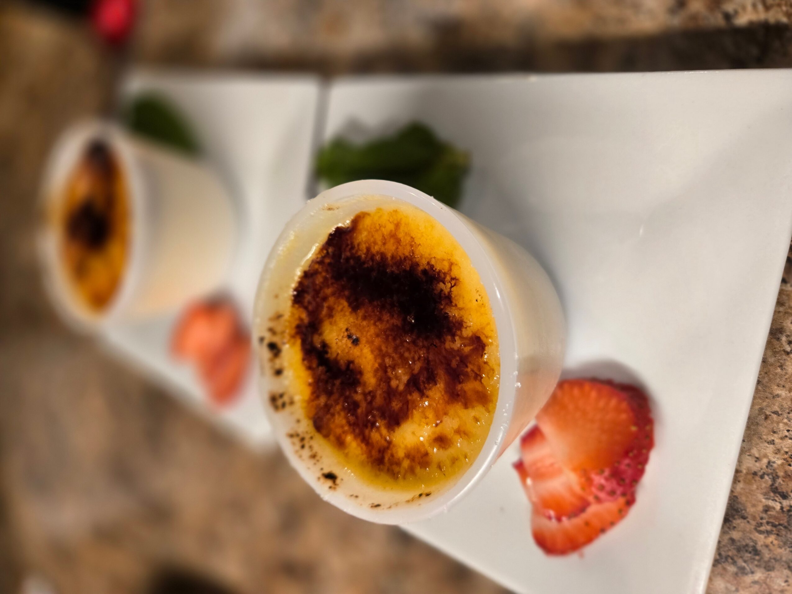 Cup of coffee with a burnt top, served with sliced strawberries on a white rectangular plate.