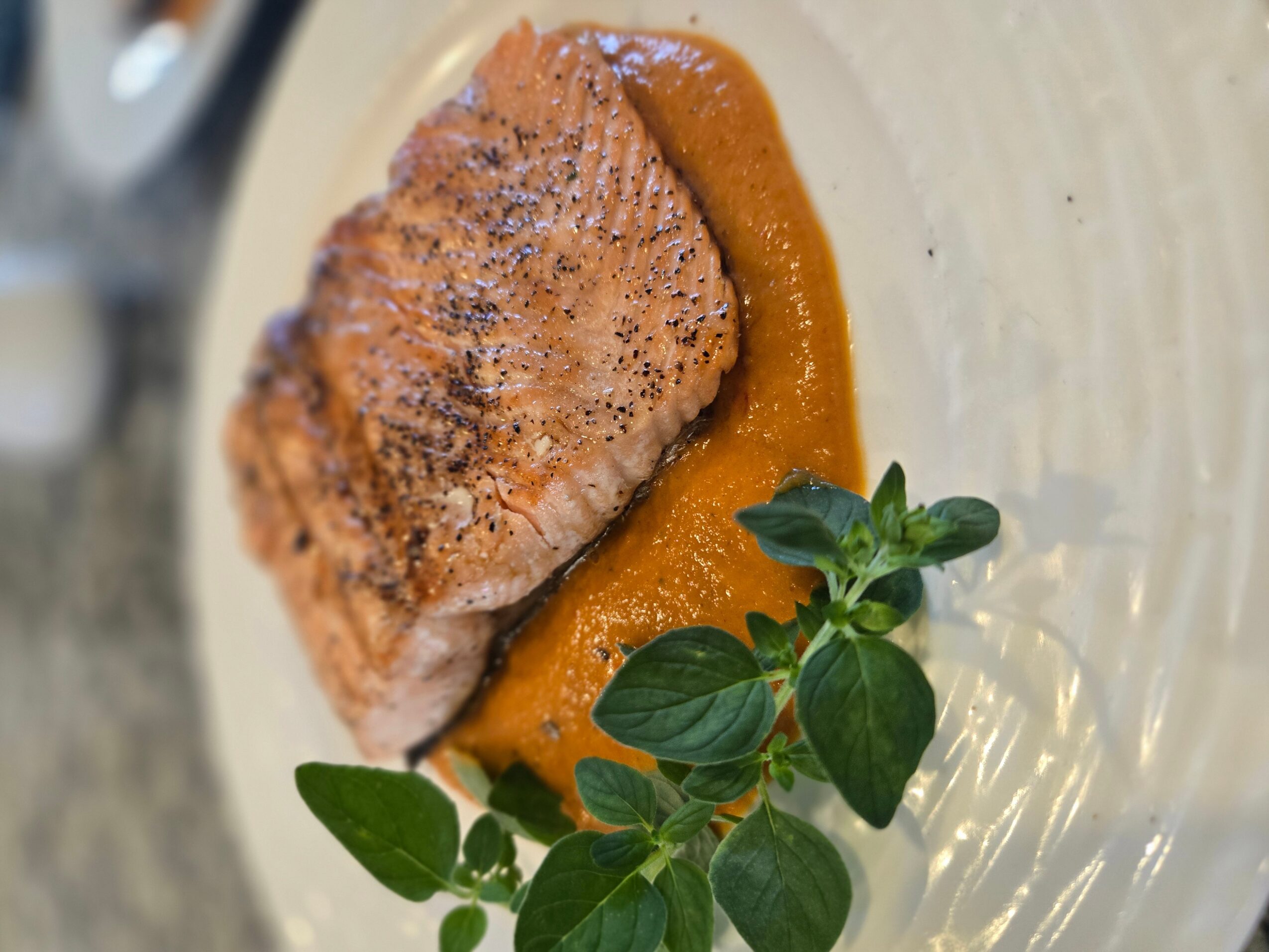 Cooked piece of meat with sauce and green herbs on a plate.