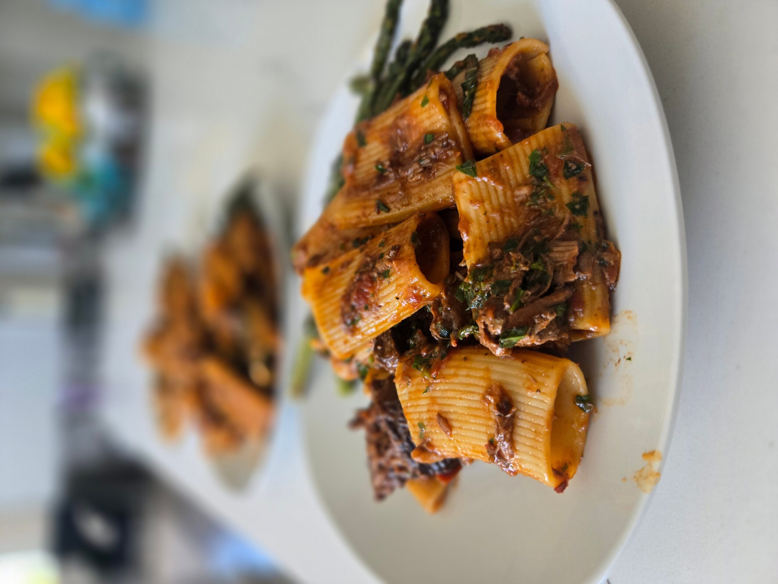 Plate with cooked pasta and vegetables, slightly tilted, on a white surface.