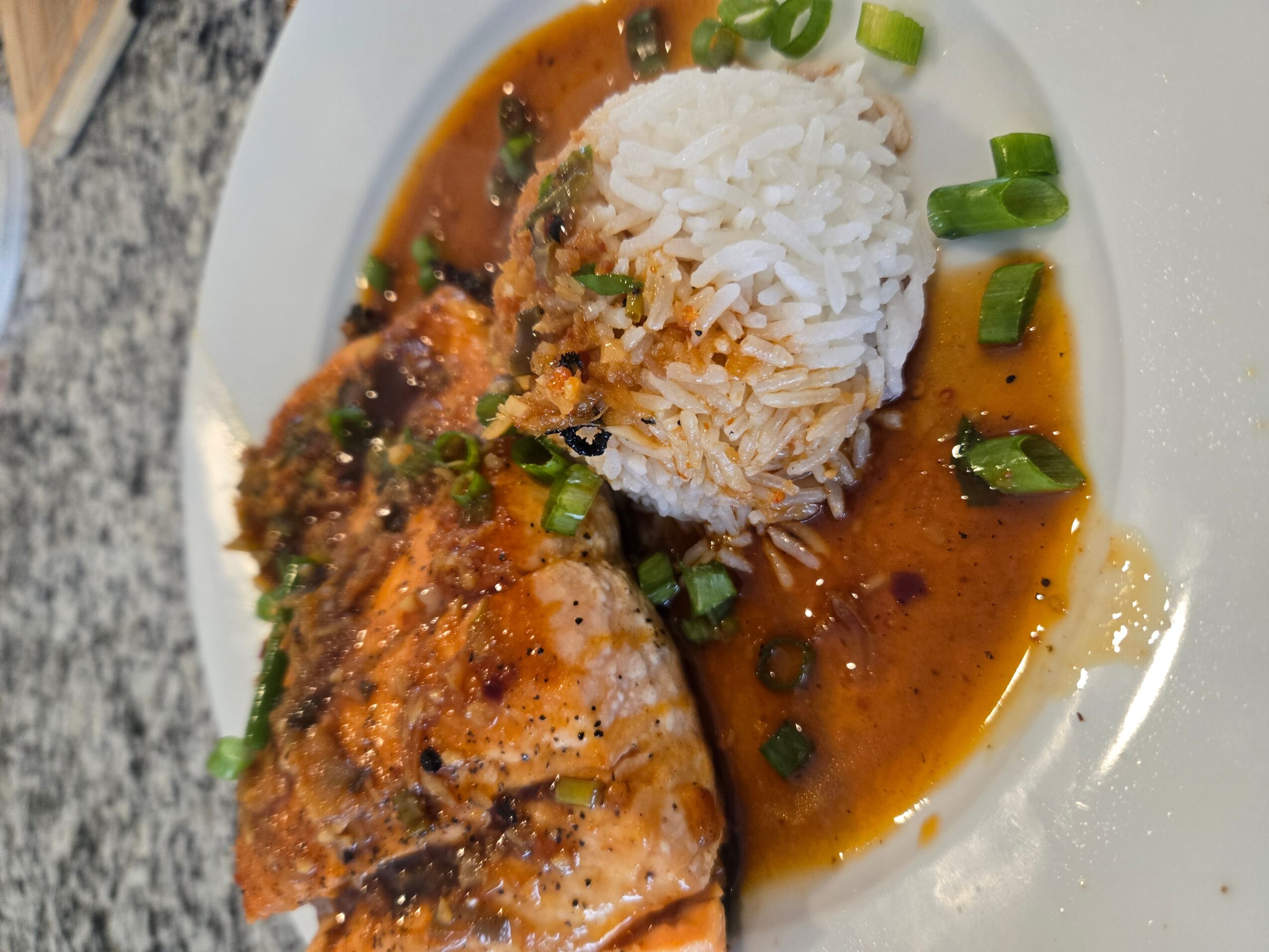 Cooked fish with rice and sauce, garnished with chopped green onions on a white plate.