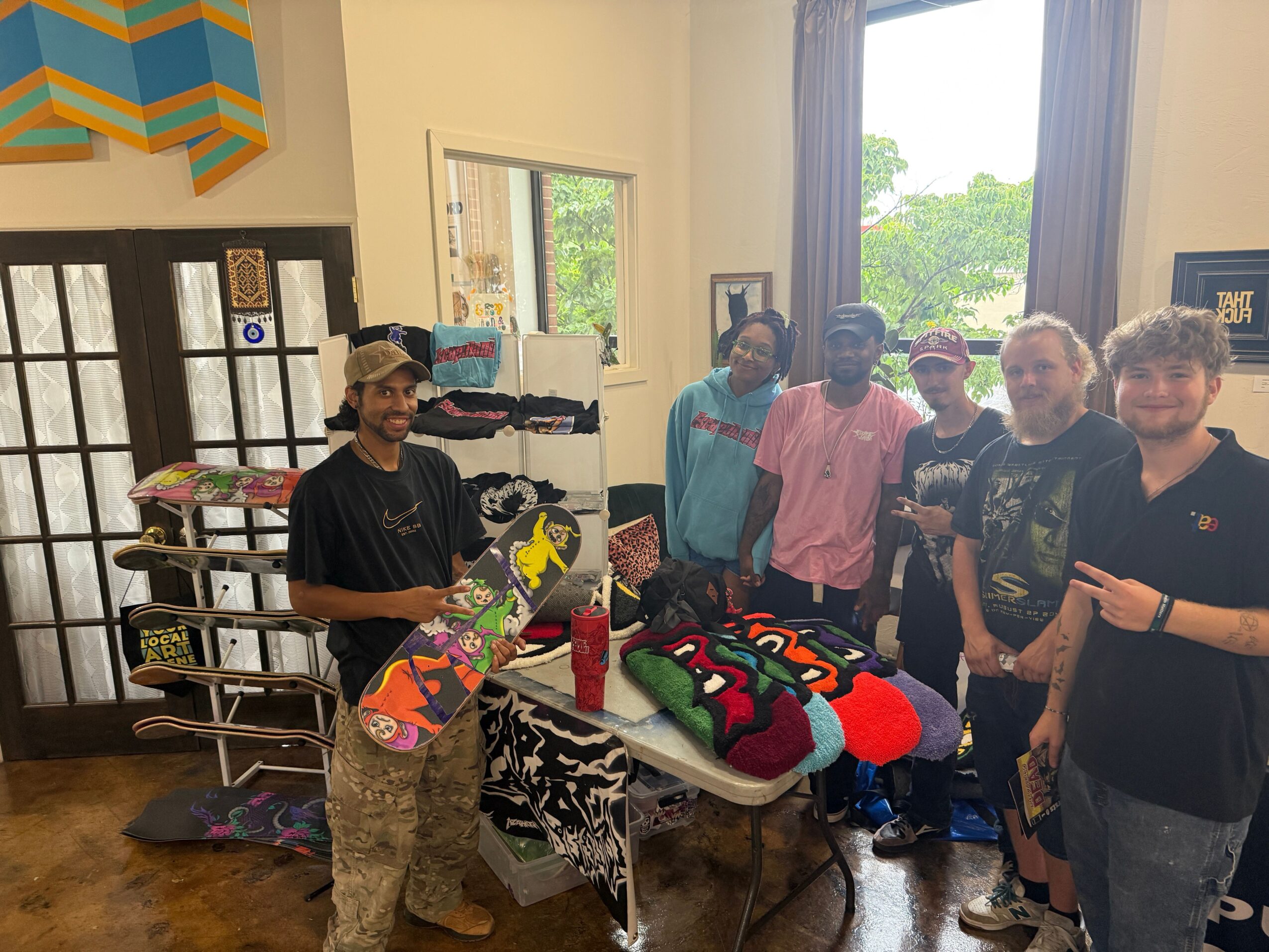 Group of children and adults in a room with toys and shelves, some children holding skateboards, others sitting or standing.