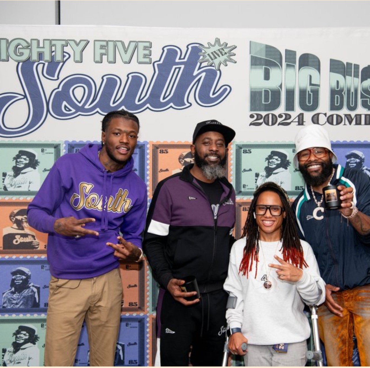 Four people standing in front of a colorful backdrop with text, smiling and posing for the photo.