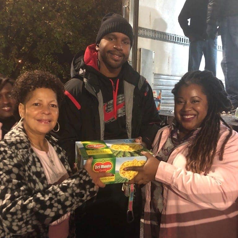 Three people smiling and holding a box of food outdoors at night.