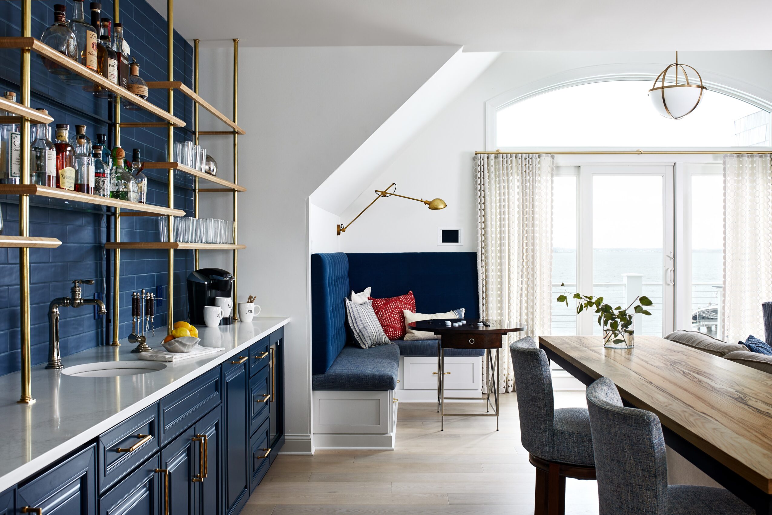 Kitchen with blue cabinets, open shelves, a dining area, and a large window with curtains, plants, and seating.