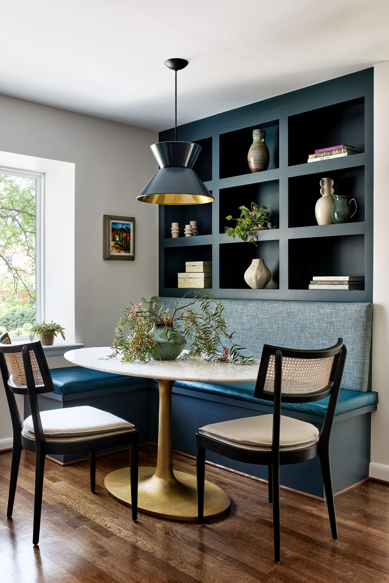 Dining nook with a round table, two chairs, a built-in bench, and a dark blue wall with open shelves holding decorative items.