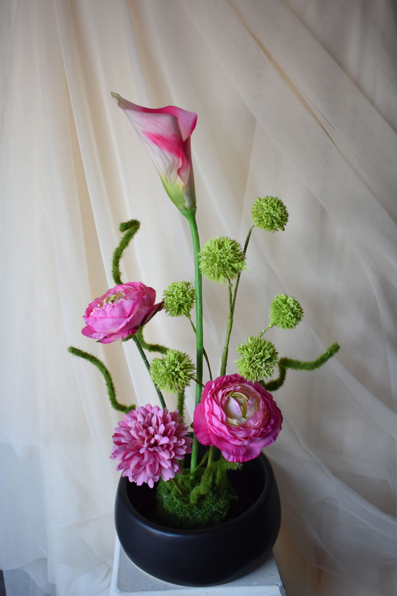 Pink and purple flowers in a black pot on a light-colored fabric background.