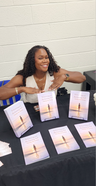 Woman with curly hair smiling and sitting at a table with books displayed in front of her.