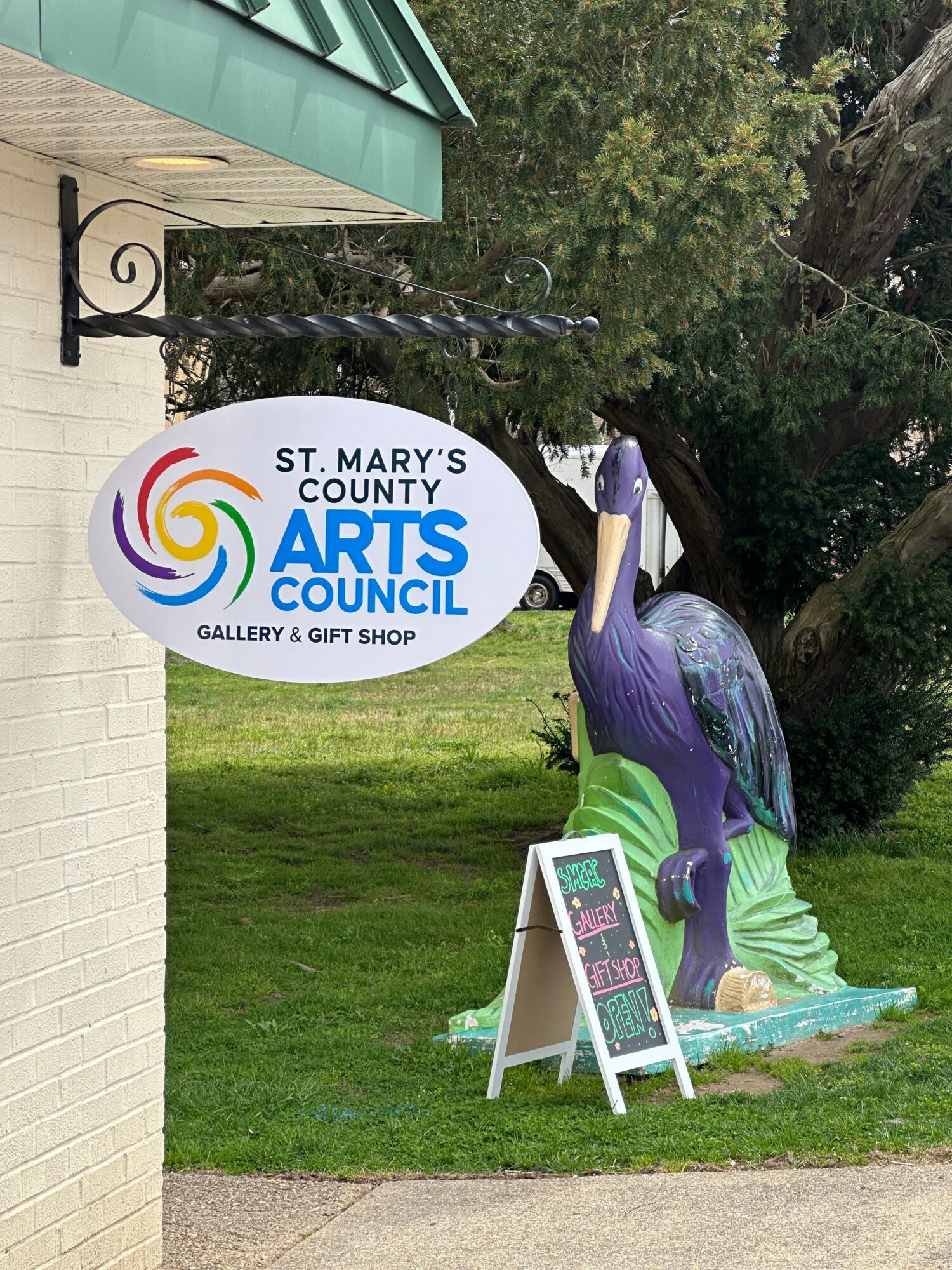 Outdoor scene with a colorful sculpture of a person, a sign for St. Mary's Arts & Culture, and a grassy area.