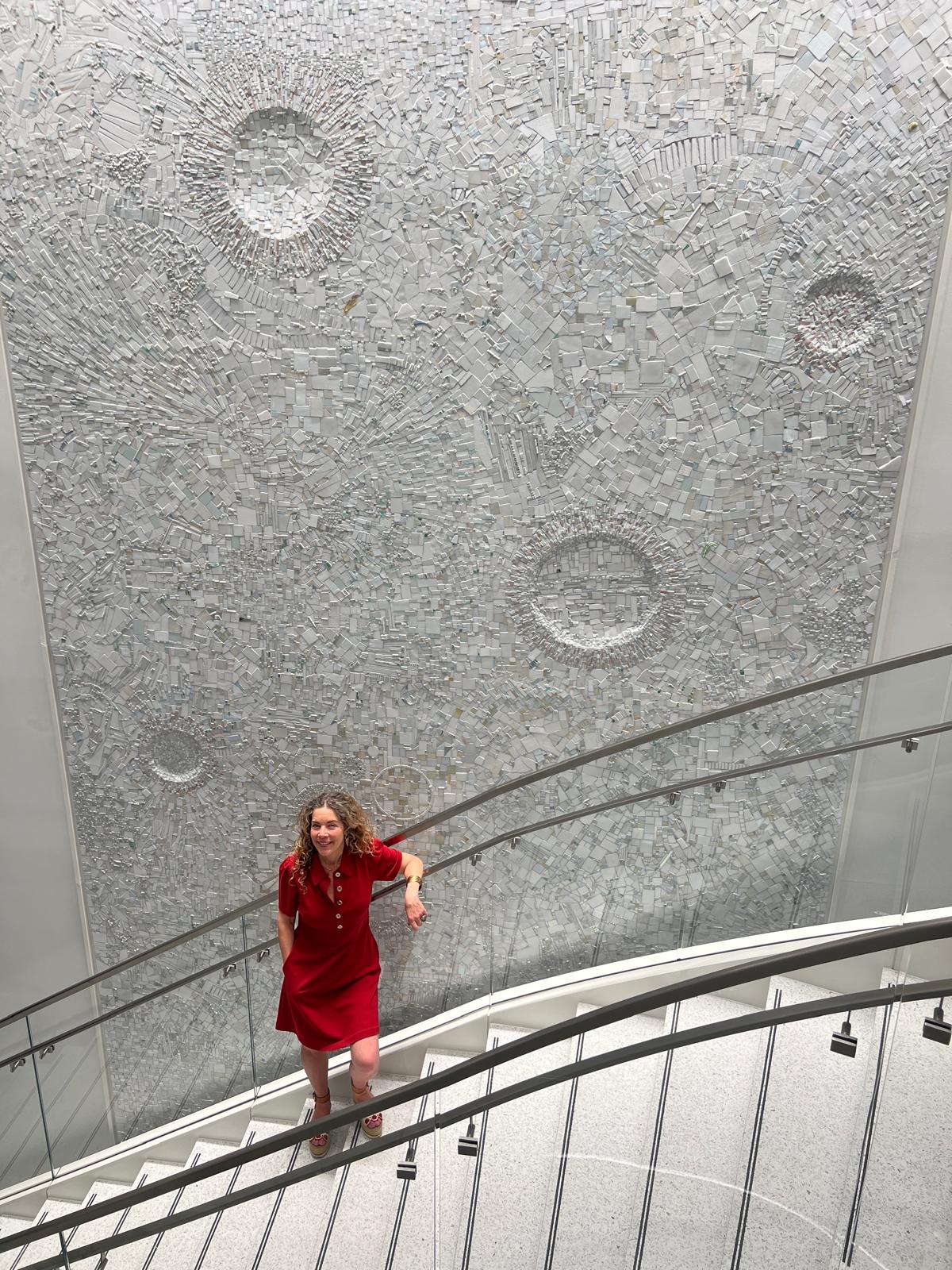 Woman in red dress standing on a staircase, looking up at a textured ceiling with circular patterns.