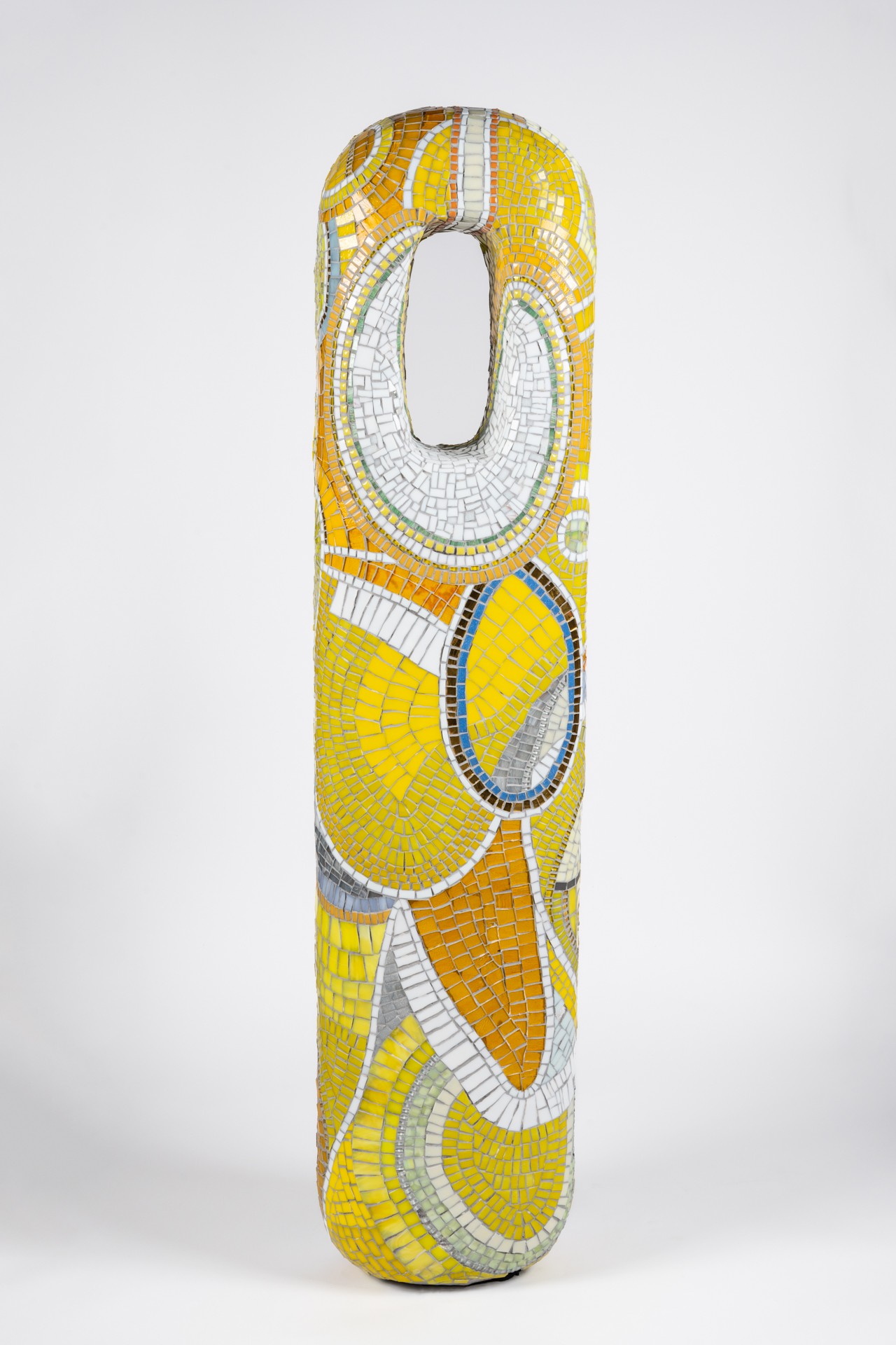 Tall, colorful abstract sculpture with yellow, white, blue, and orange patterns, standing upright against a plain white background.