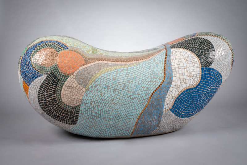 Colorful mosaic sculpture resembling a bean shape with various patterns and colors, on a plain background.