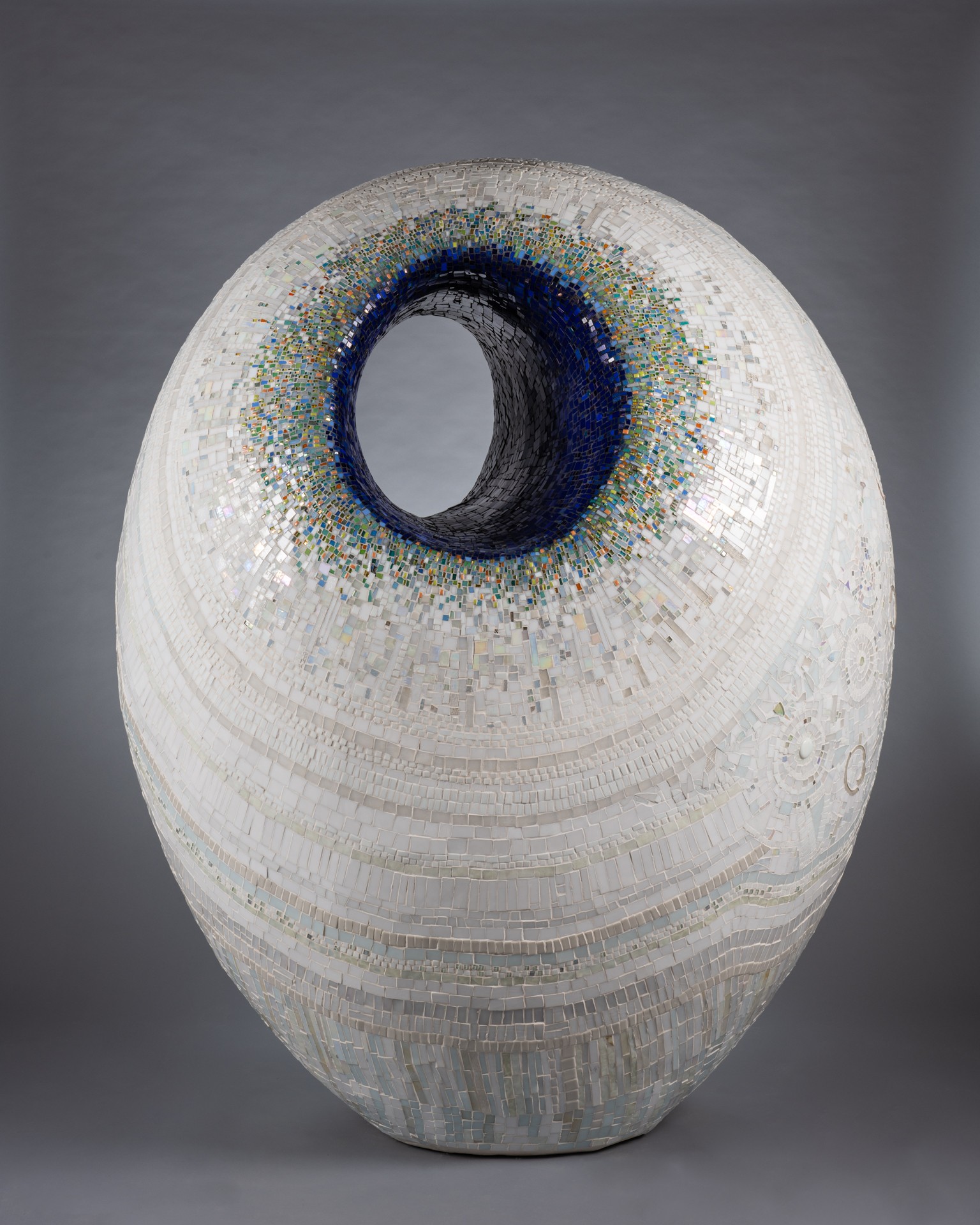 Ceramic vase with a circular opening, decorated with blue and green speckles around the opening, on a gray background.