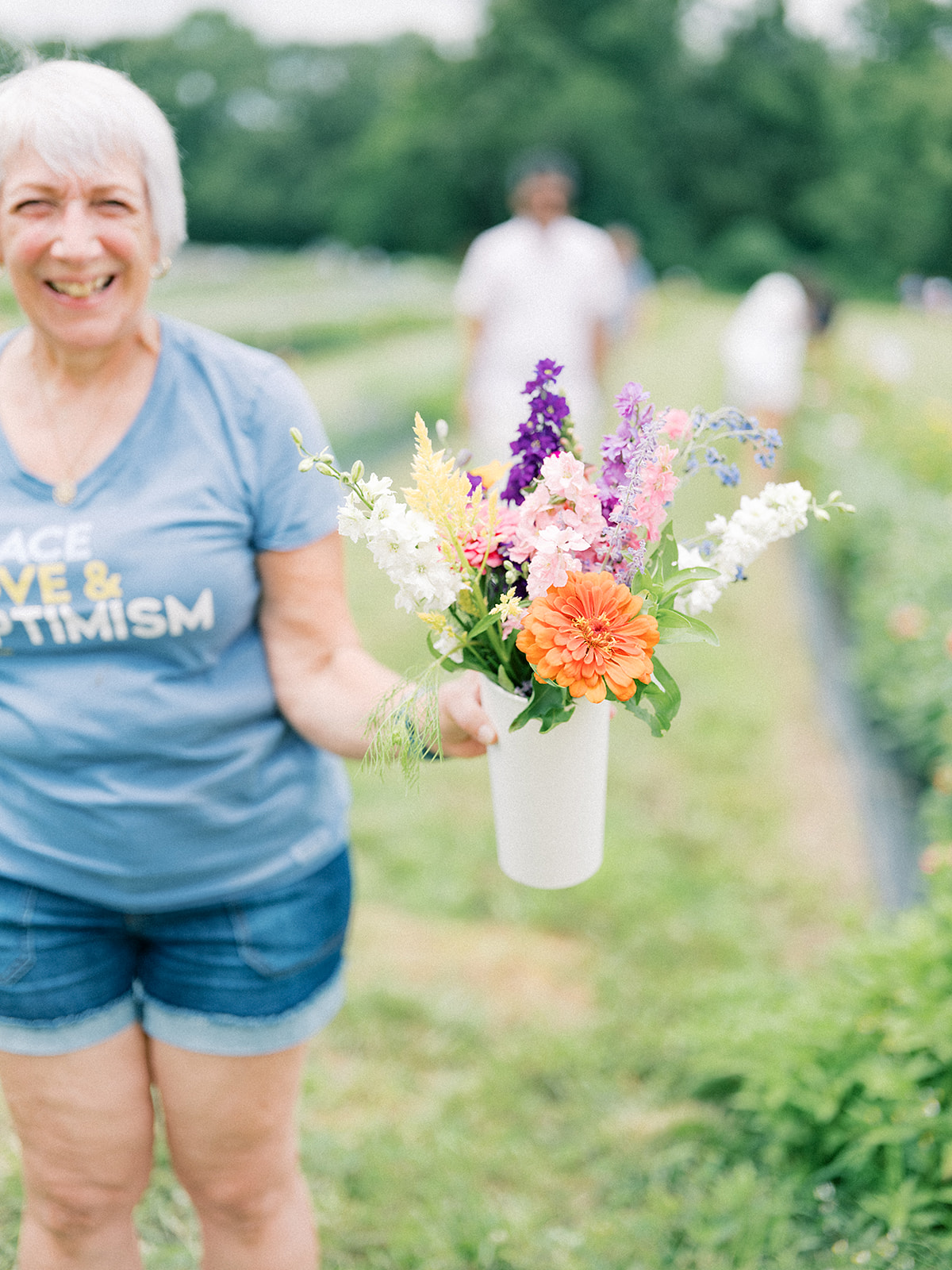 Smiling elderly woman holding a colorful flower bouquet outdoors in a park.