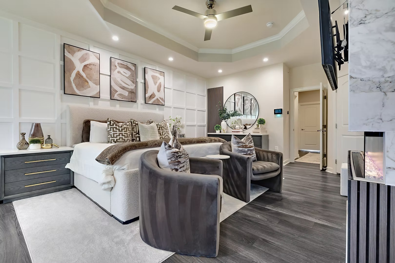 Living room with a large bed, four chairs, wall art, and a ceiling fan, with dark wood flooring and light walls.