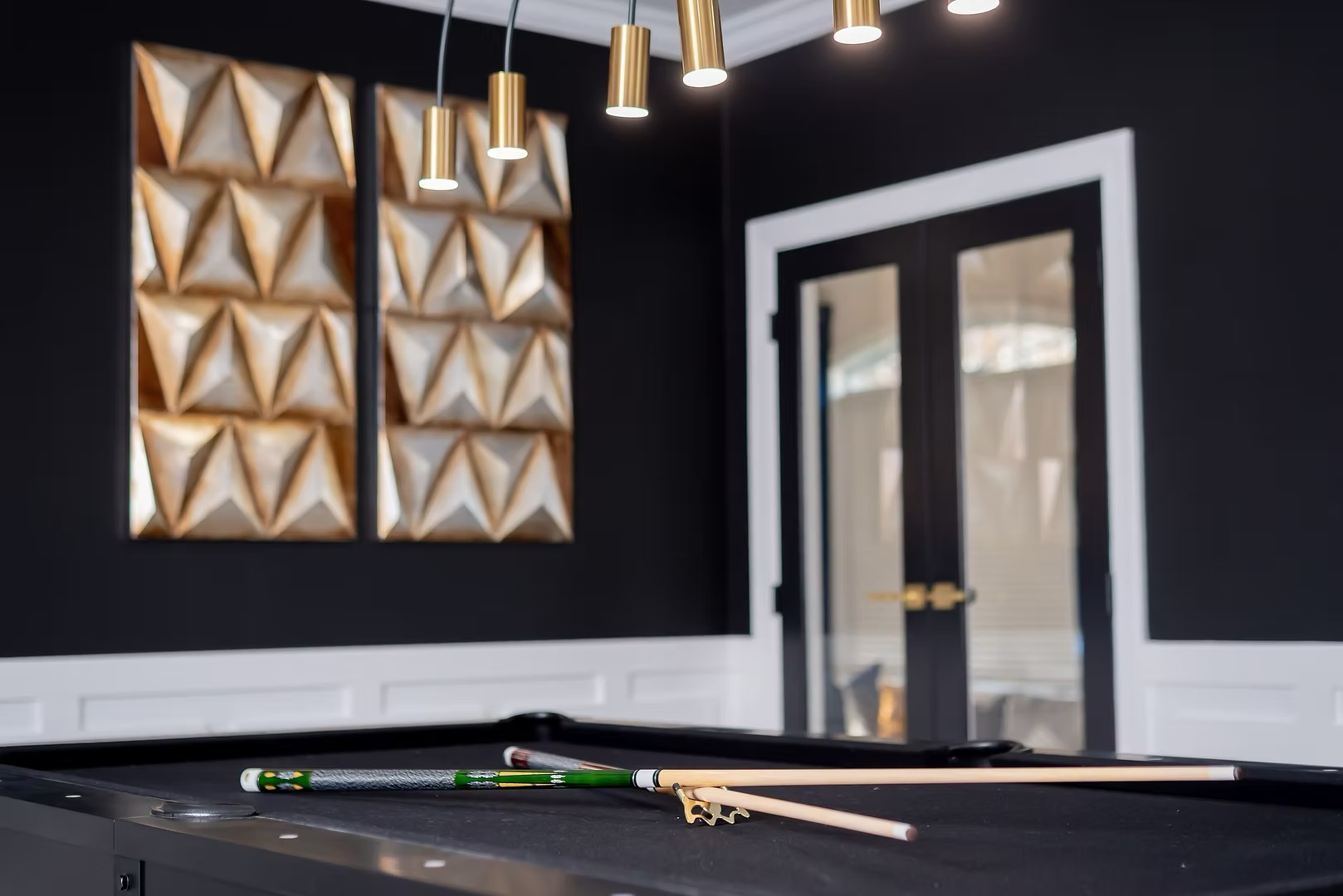 Interior room with black walls, gold pendant lights, decorative wall art, and a door with glass panels.