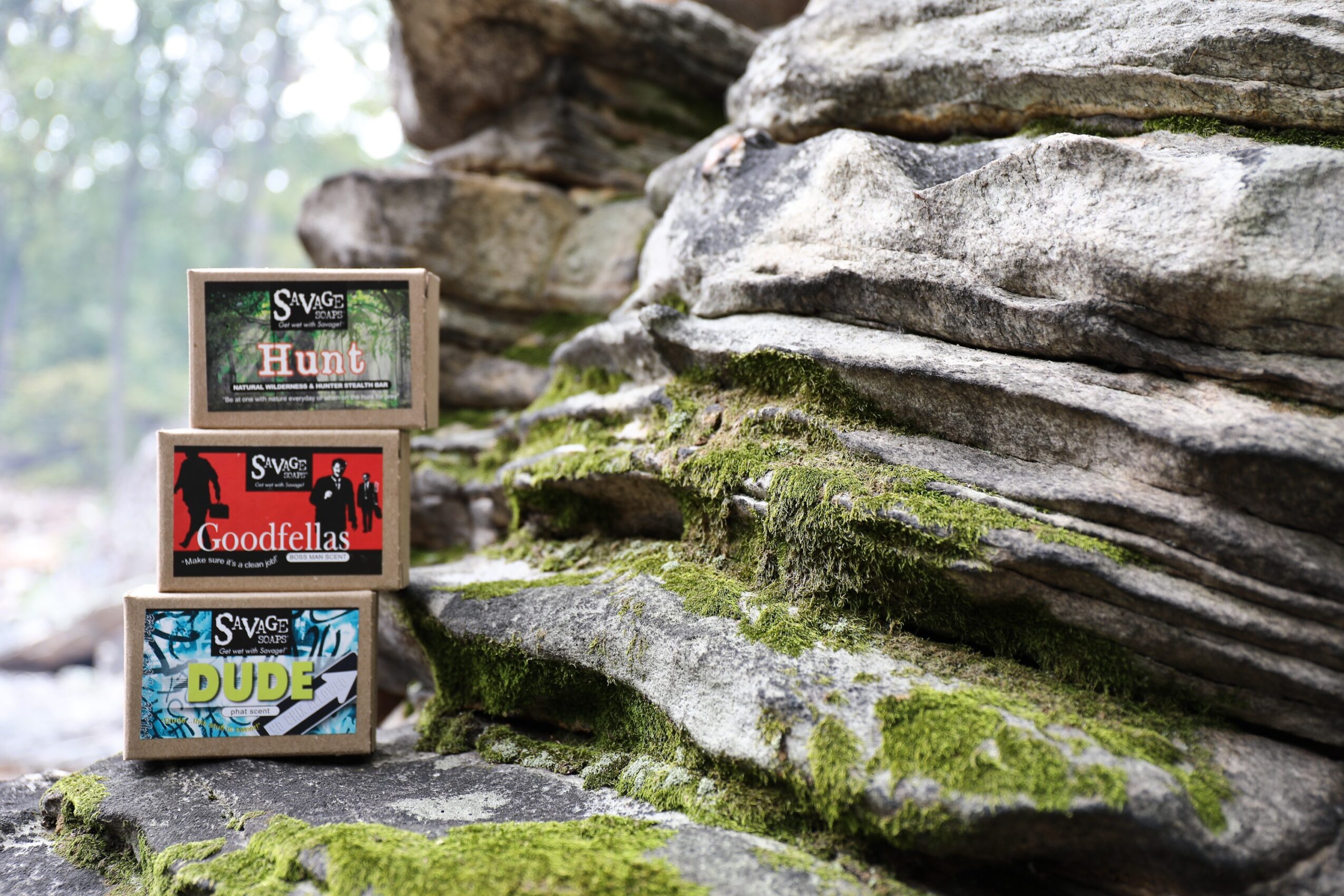 Three stacked boxes with game titles in front of a mossy rock formation outdoors.