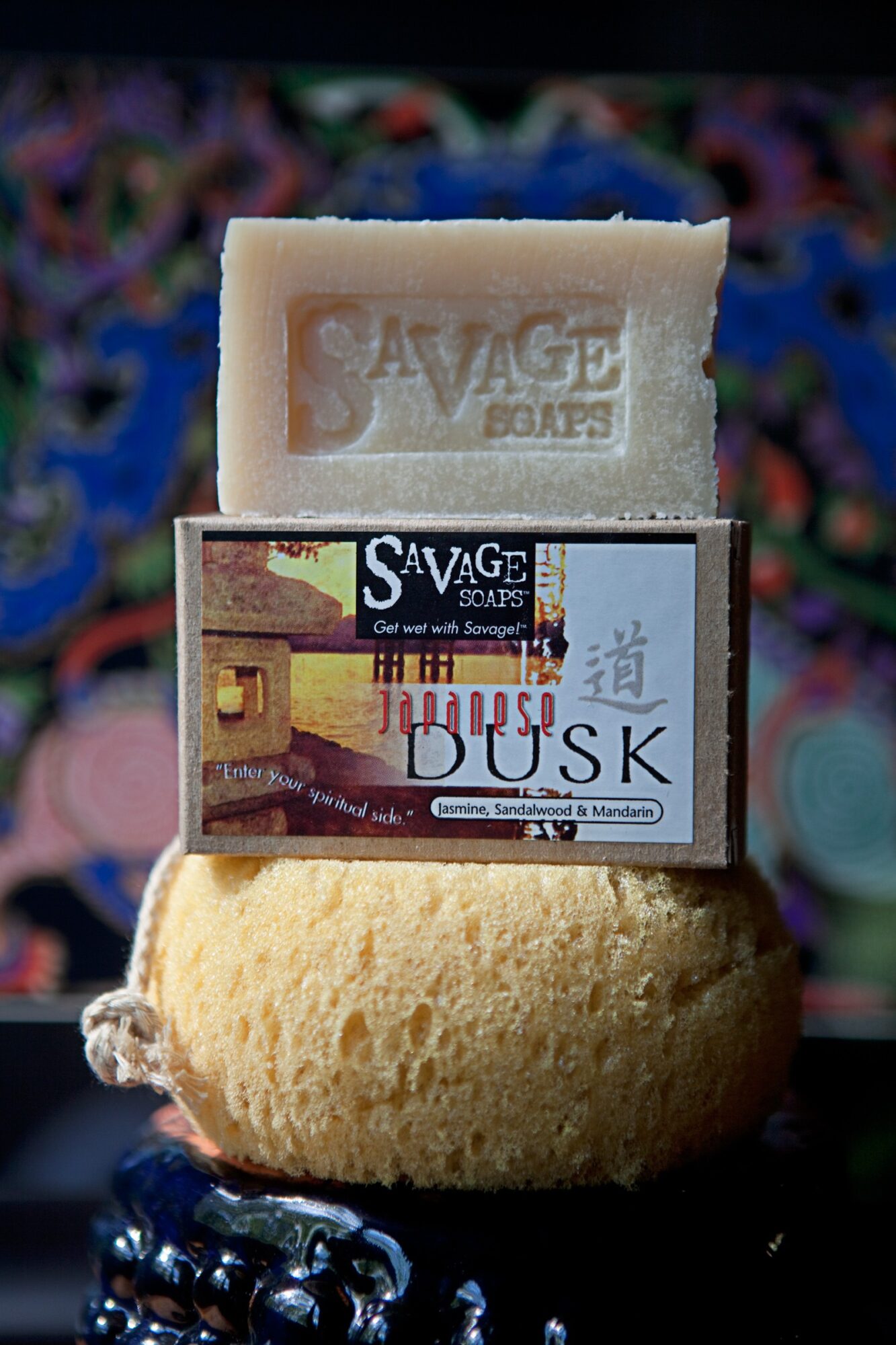 Stack of soap bars with a label reading 'Dusk' and a beige soap with embossed text, against a colorful background.