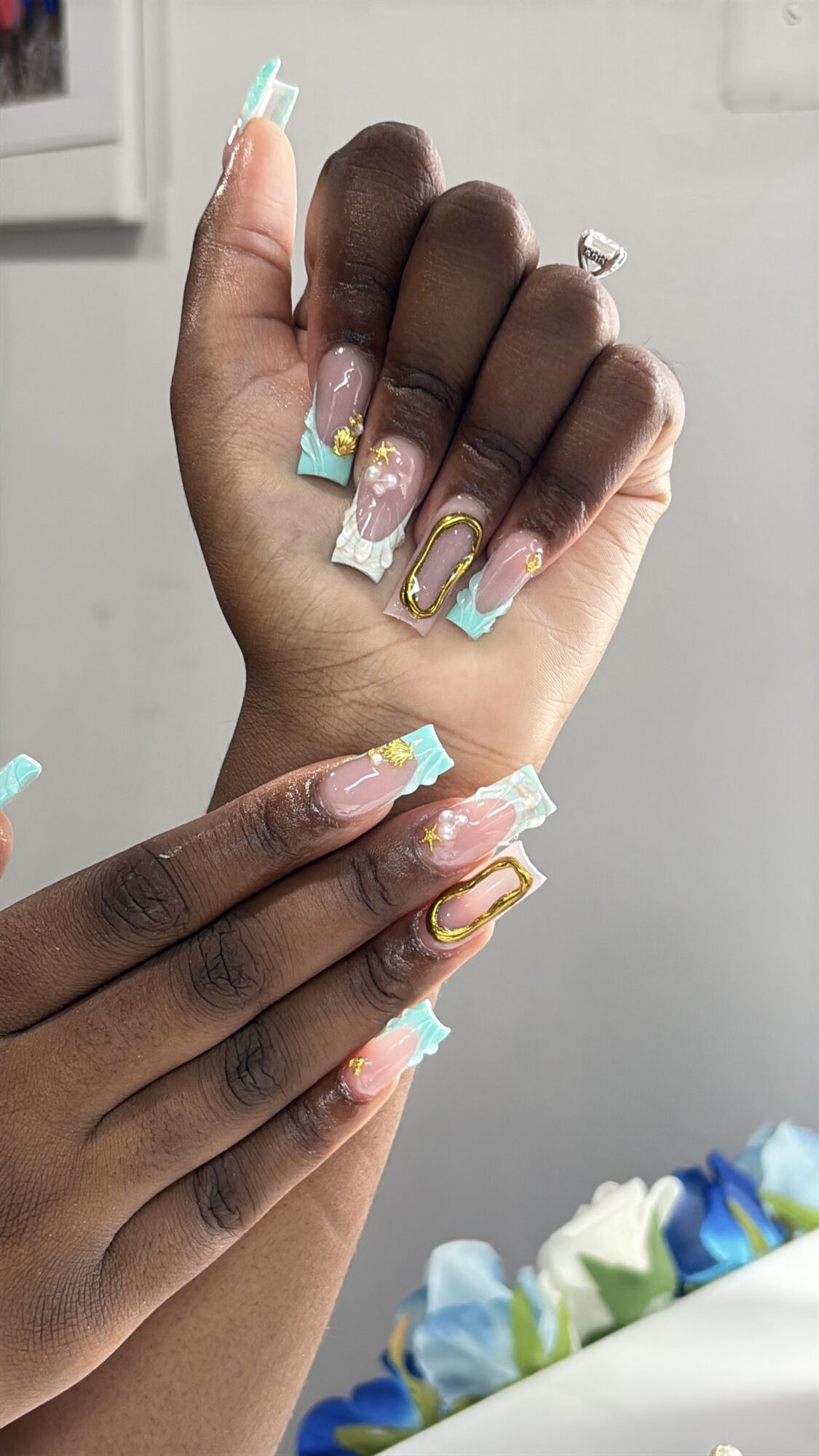 Two hands with colorful, decorated nails, one with darker skin and the other with lighter skin, against a neutral background.