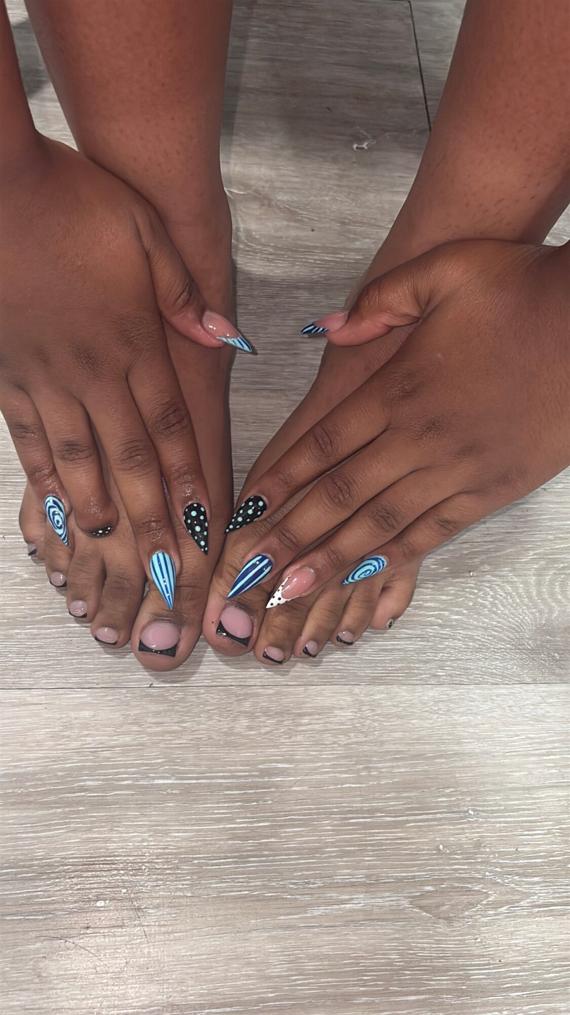 Two pairs of hands and feet with decorated nails touching on a wooden floor.