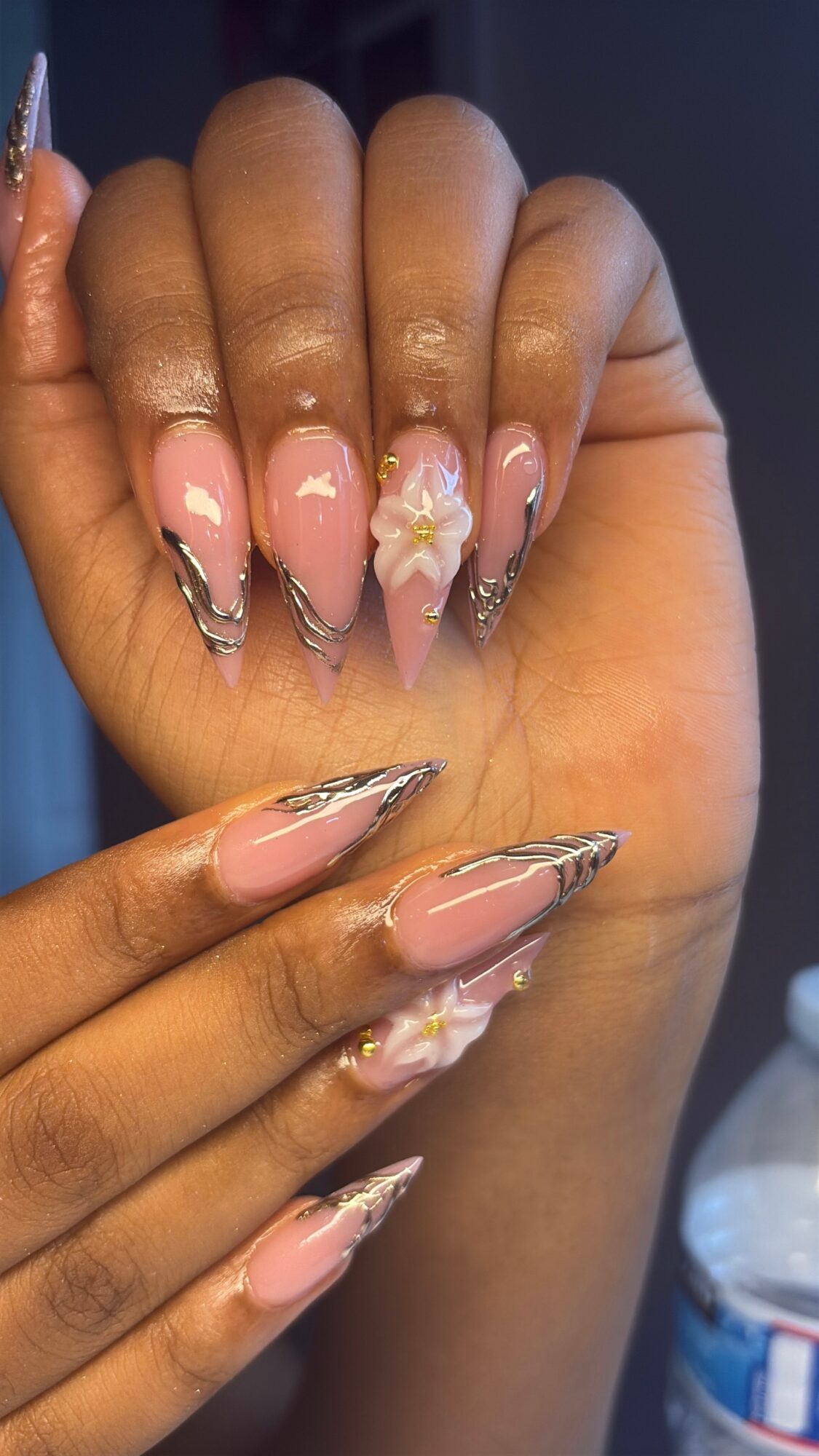 Close-up of hands with decorated nails, featuring pink polish, floral designs, and metallic accents.