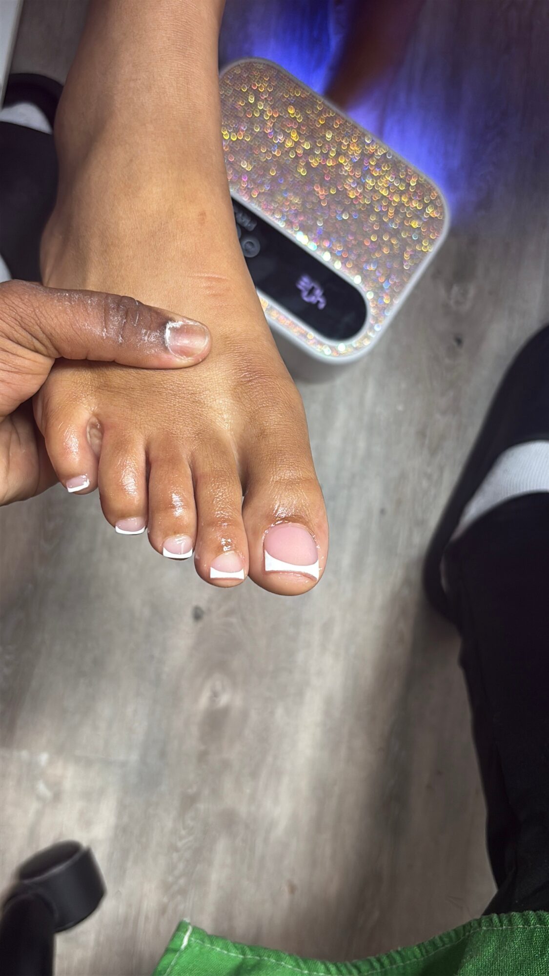 Person's foot being held, with a glittery, illuminated device nearby, on a wooden floor.