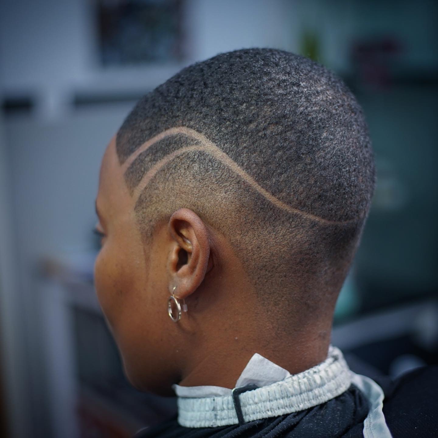 Side view of a person with a short, textured haircut and decorative lines shaved into the side of the head.