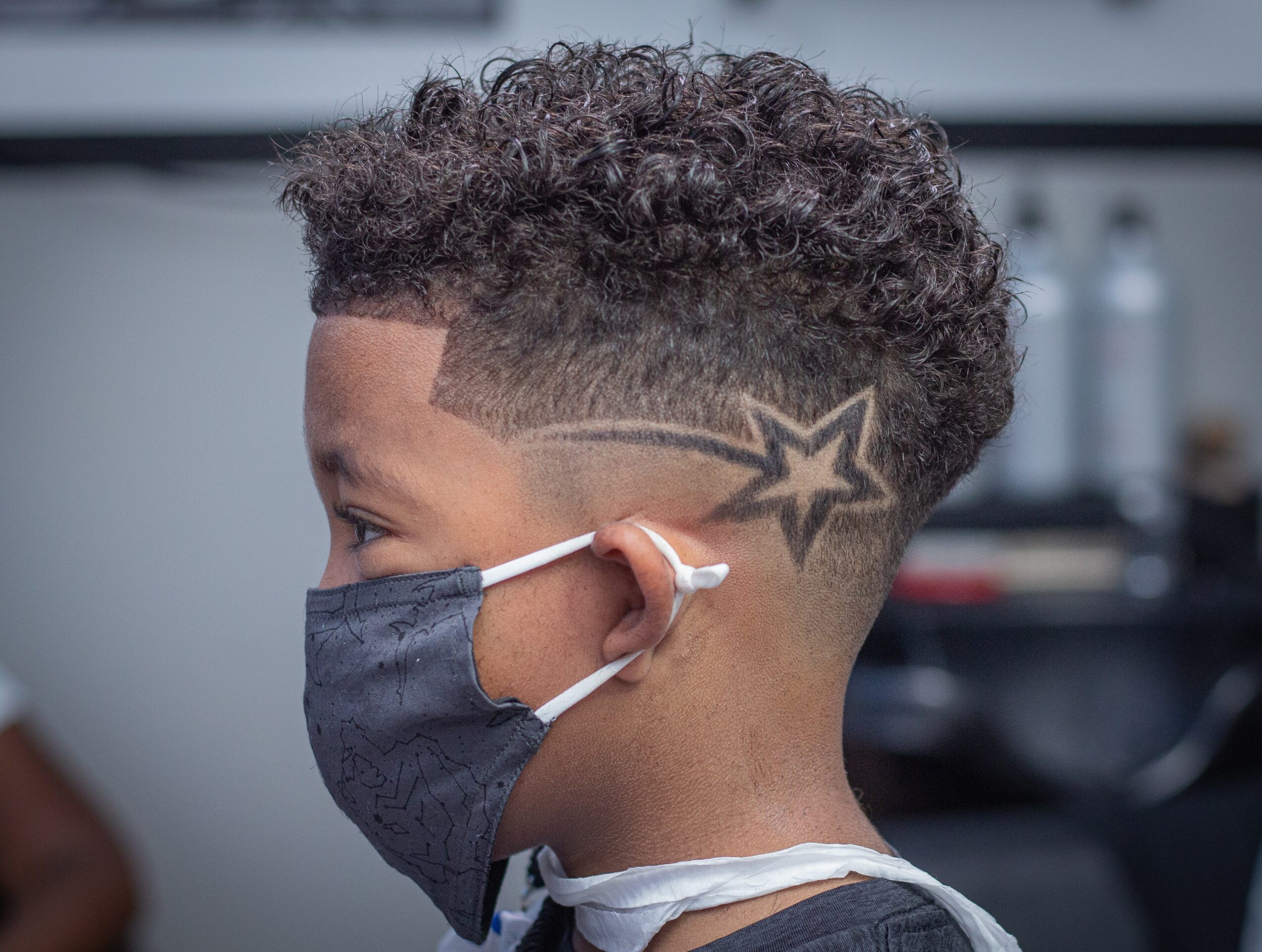 Side profile of a person with curly hair, star tattoo on the side of their head, wearing a face mask.
