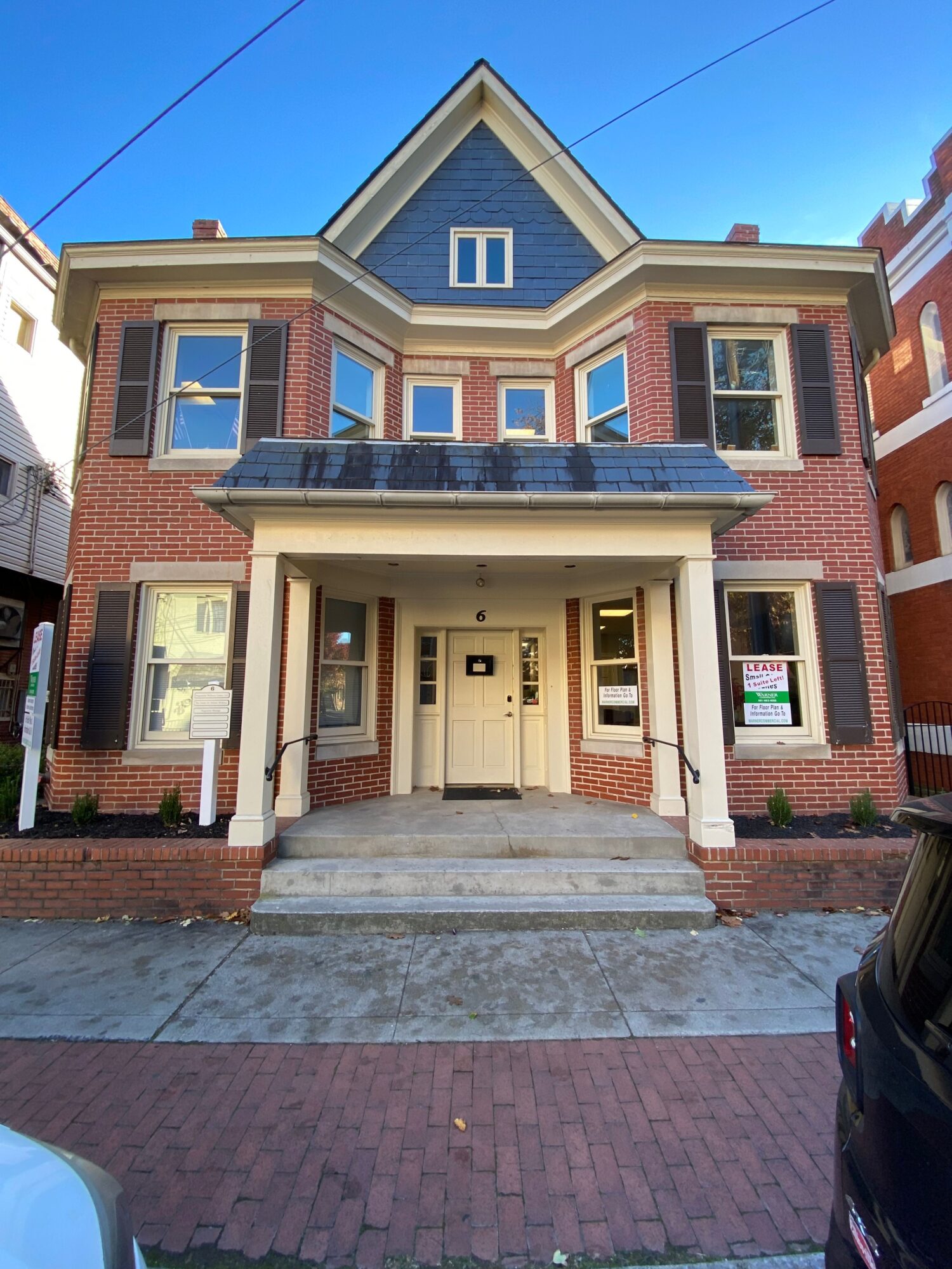 Two-story brick house with front porch, windows, and a small front yard, viewed from the sidewalk.