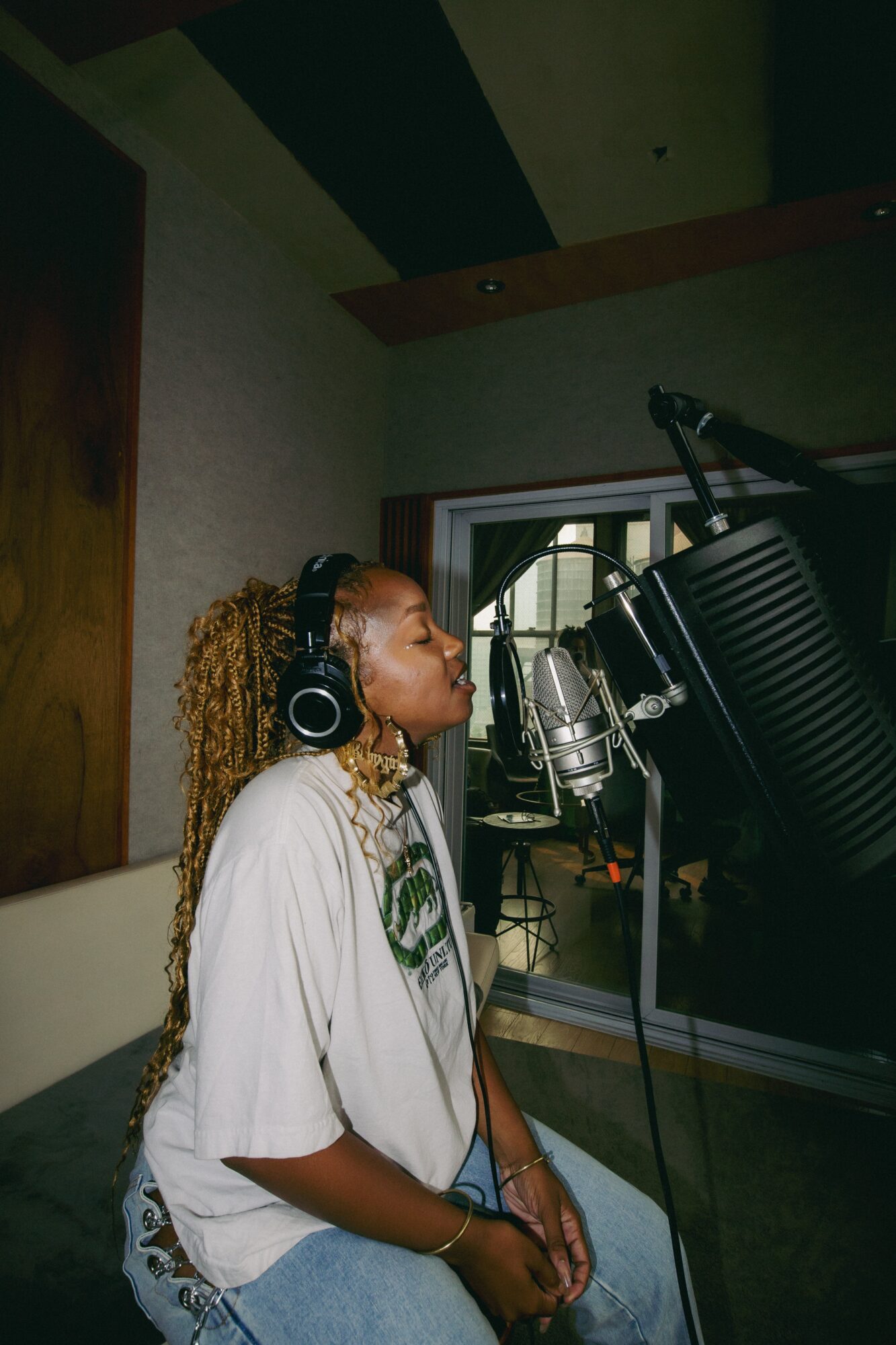 Woman with curly hair wearing headphones singing into a microphone in a recording studio.