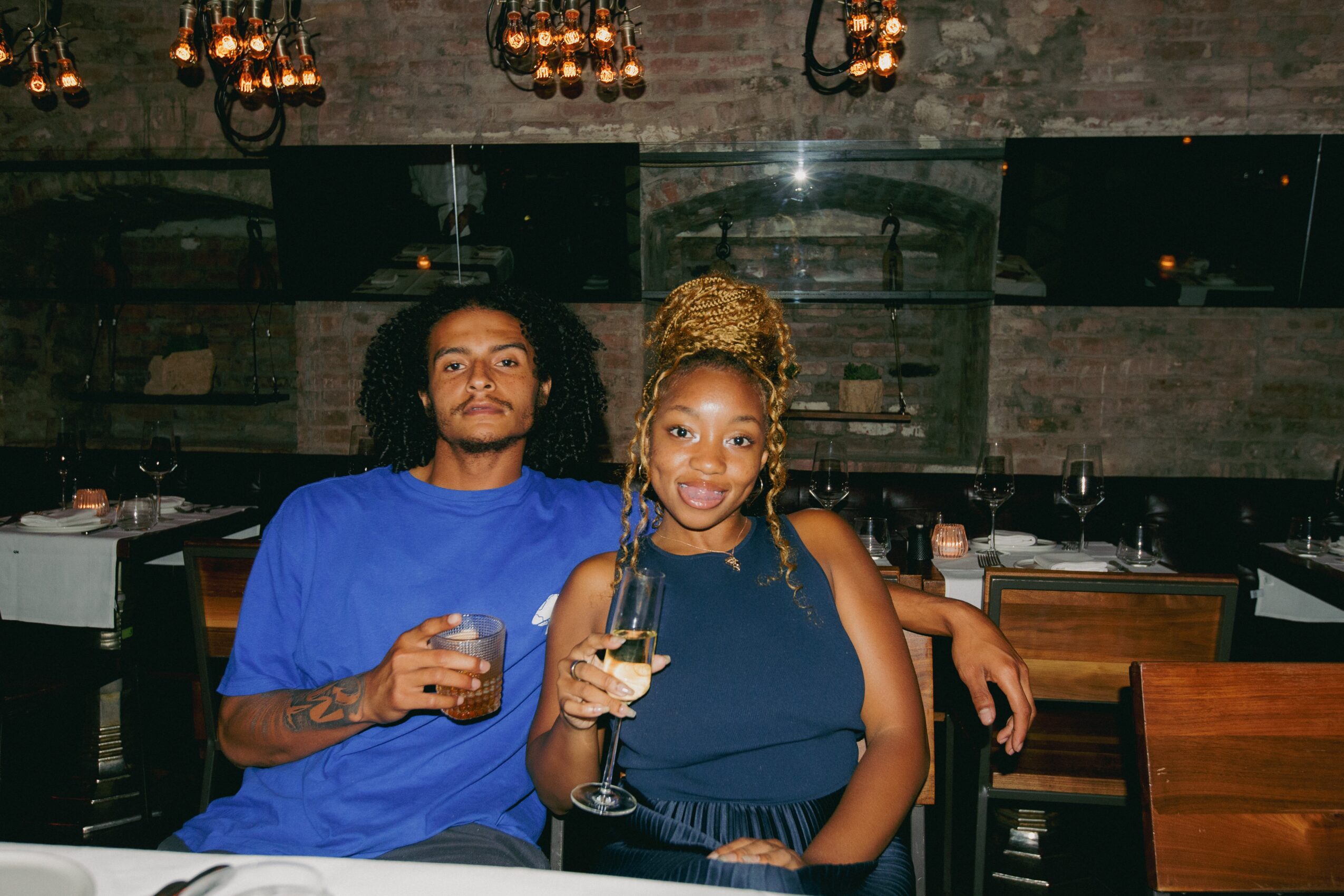 Two women sitting at a table in a dimly lit restaurant, holding drinks and smiling.