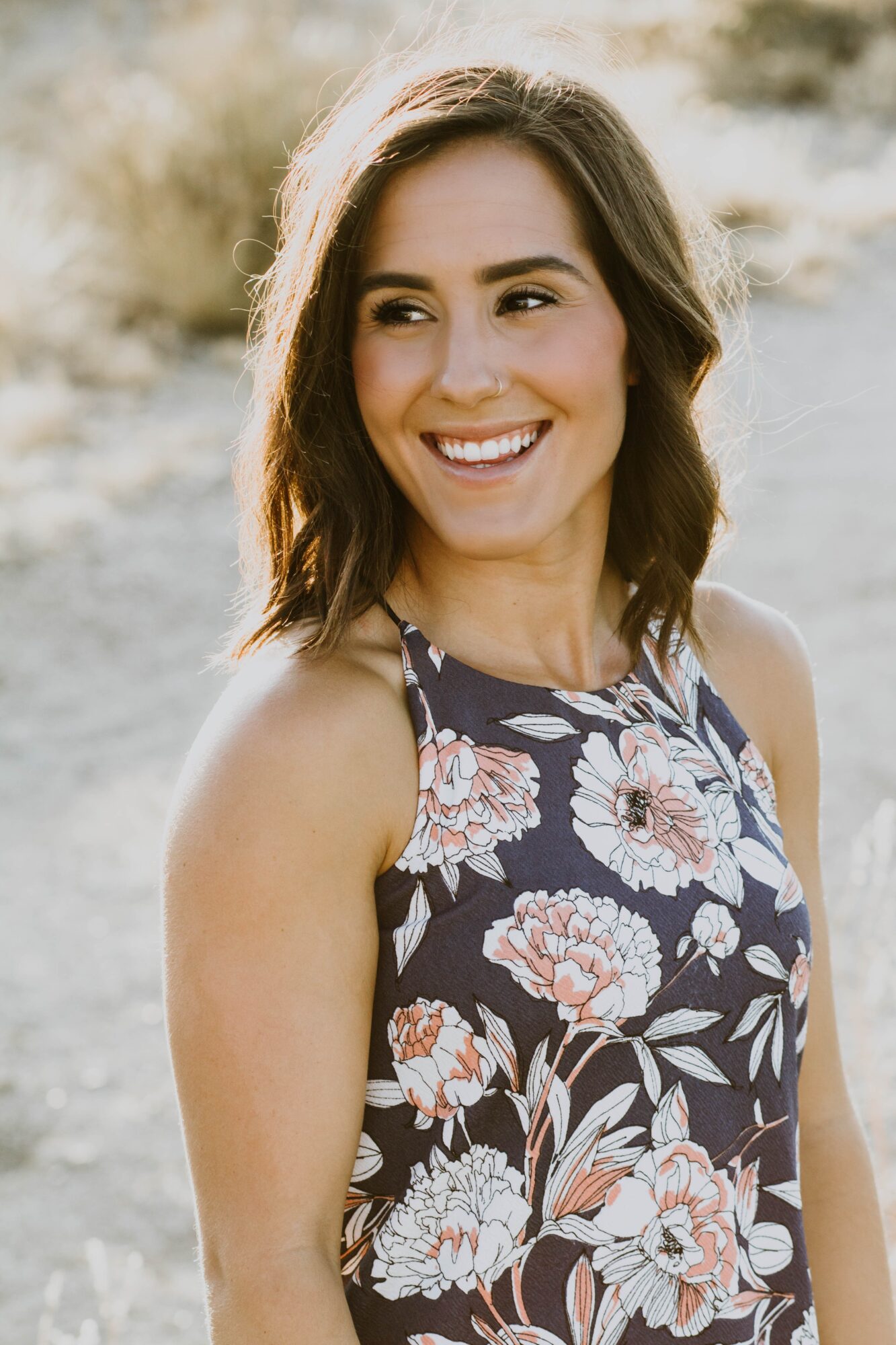 Smiling woman with shoulder-length dark hair wearing a floral sleeveless top outdoors.