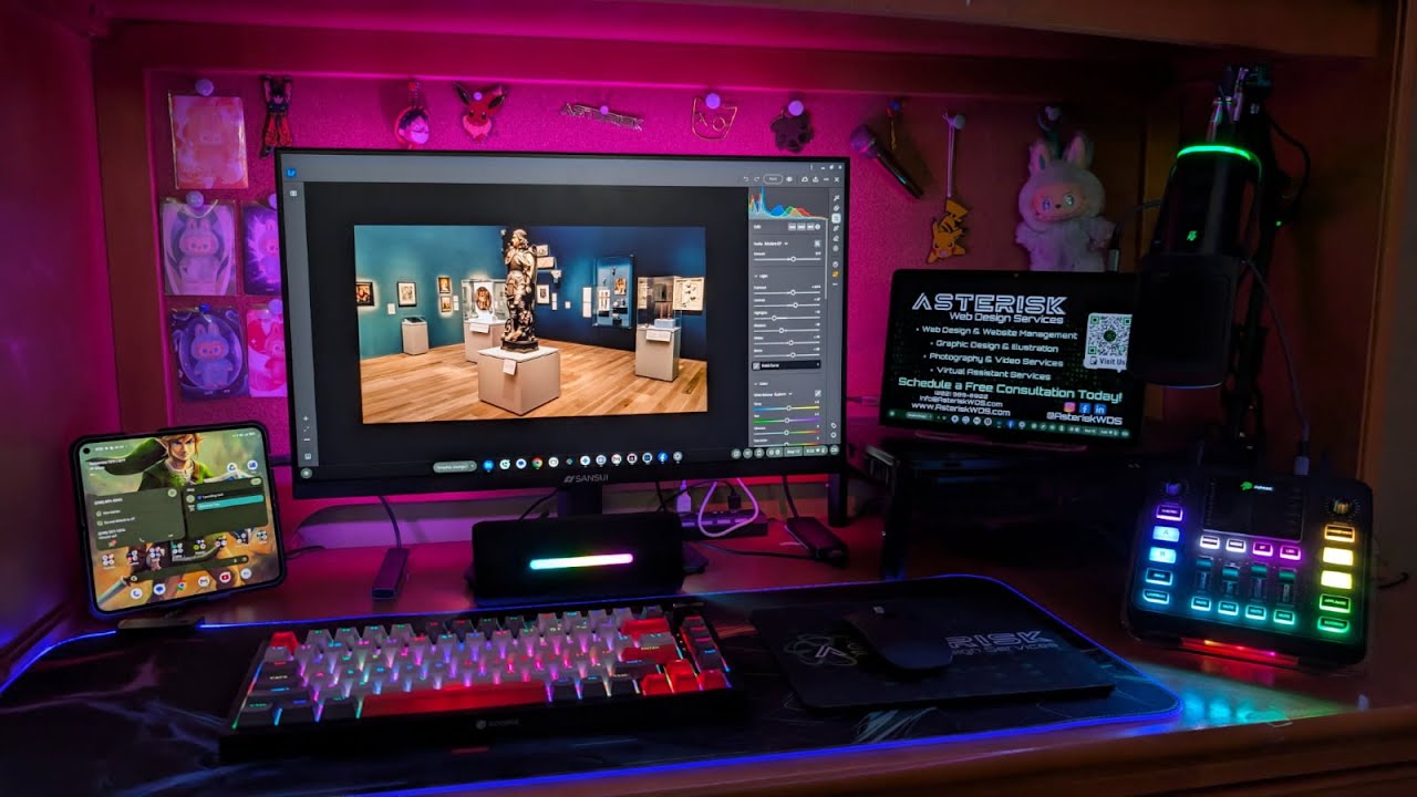 Computer setup with monitor, keyboard, tablet, and colorful lighting on a desk, with a decorated background.