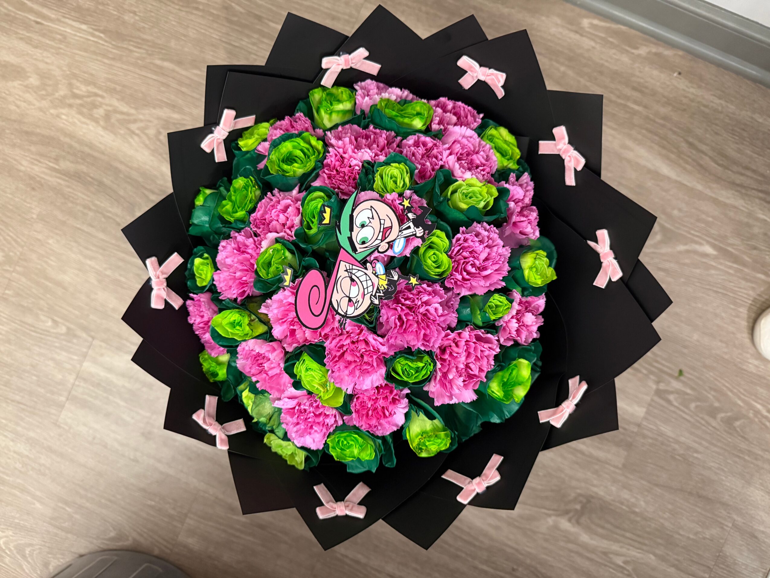 Bouquet of pink and green flowers with a butterfly decoration, wrapped in black paper with pink bows, on a wooden surface.