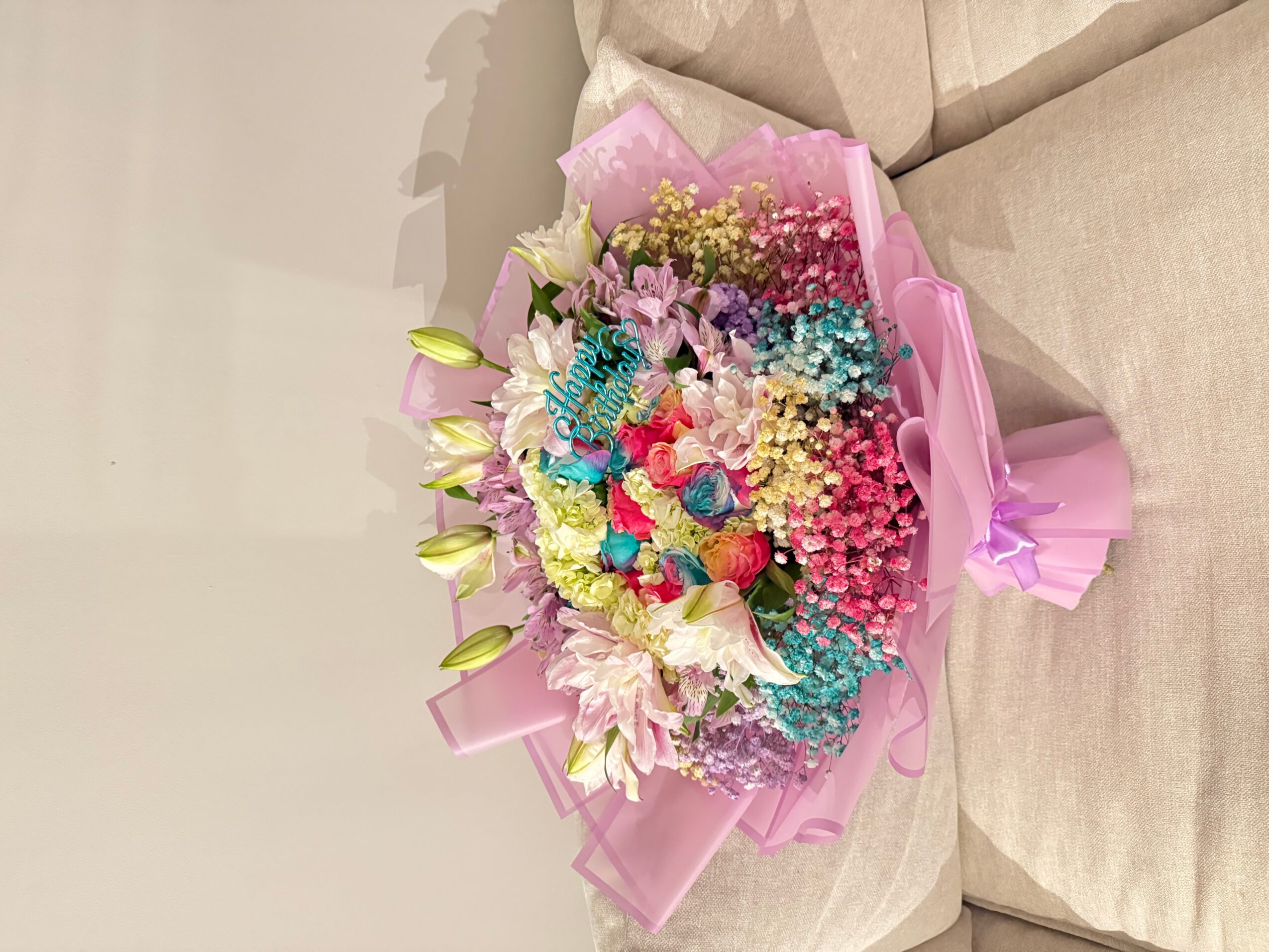 Colorful bouquet of flowers wrapped in pink paper, resting on a beige sofa.