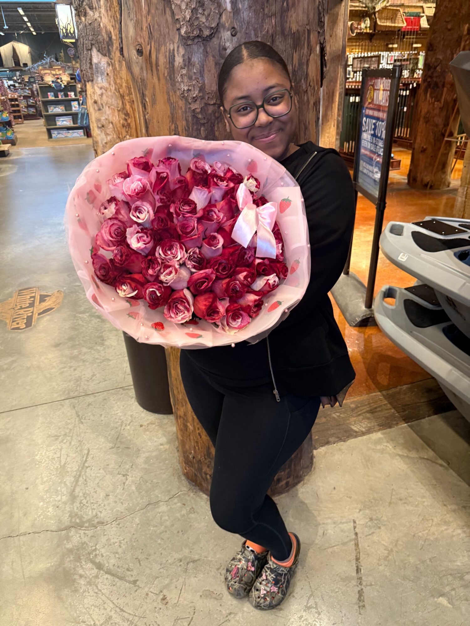 Woman holding a large bouquet of pink and red roses in a store, smiling at the camera.