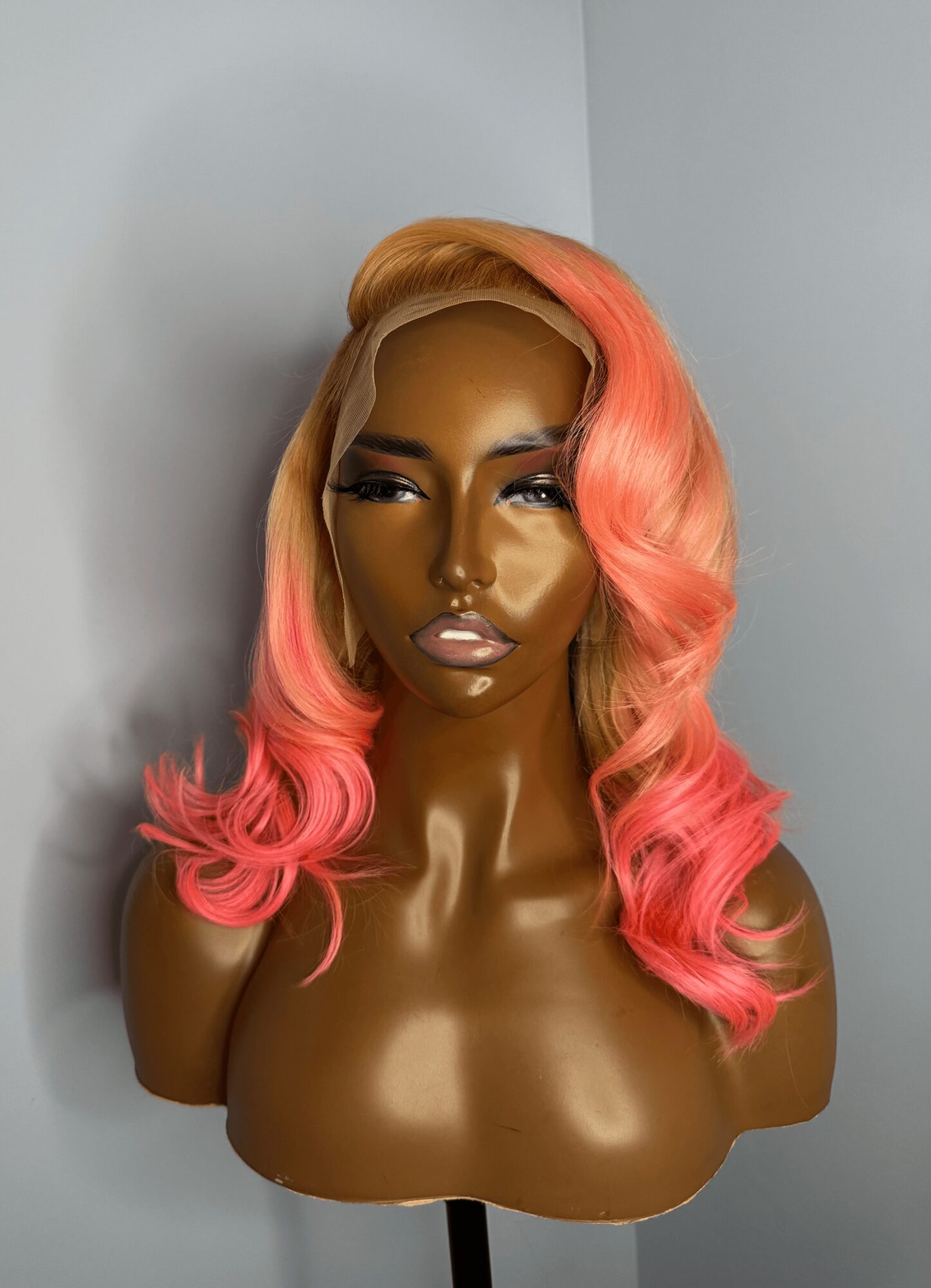 Bust of a woman with long, wavy hair in shades of pink and orange, with makeup and a neutral expression.