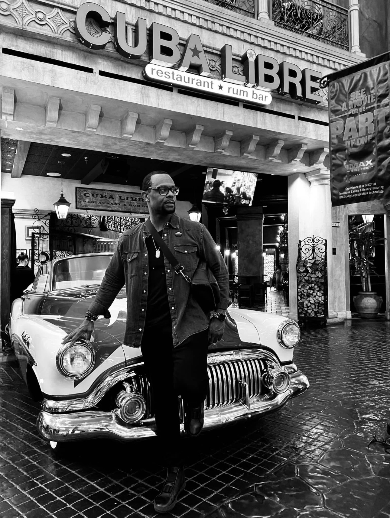 Man standing in front of a vintage car outside a restaurant named Cub Libre, with signage and street scene visible.