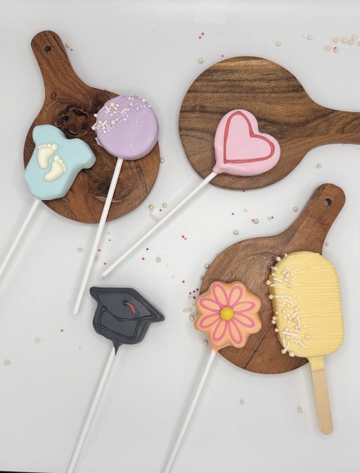Assorted decorated cookies on wooden paddles, including a heart, flower, and baby-themed cookies, with a yellow brush-shaped cookie.