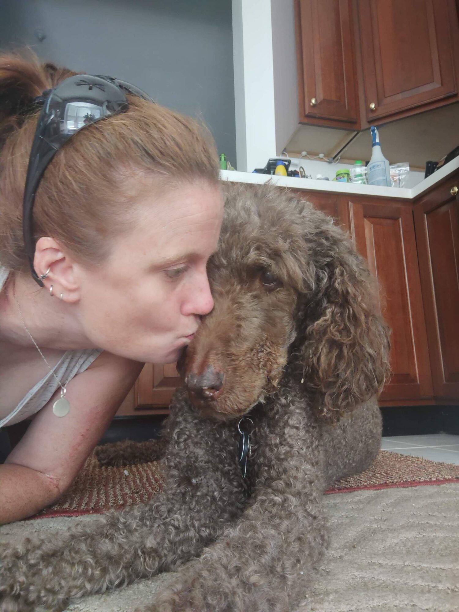 Girl with headphones kisses a curly-haired dog on the nose indoors.