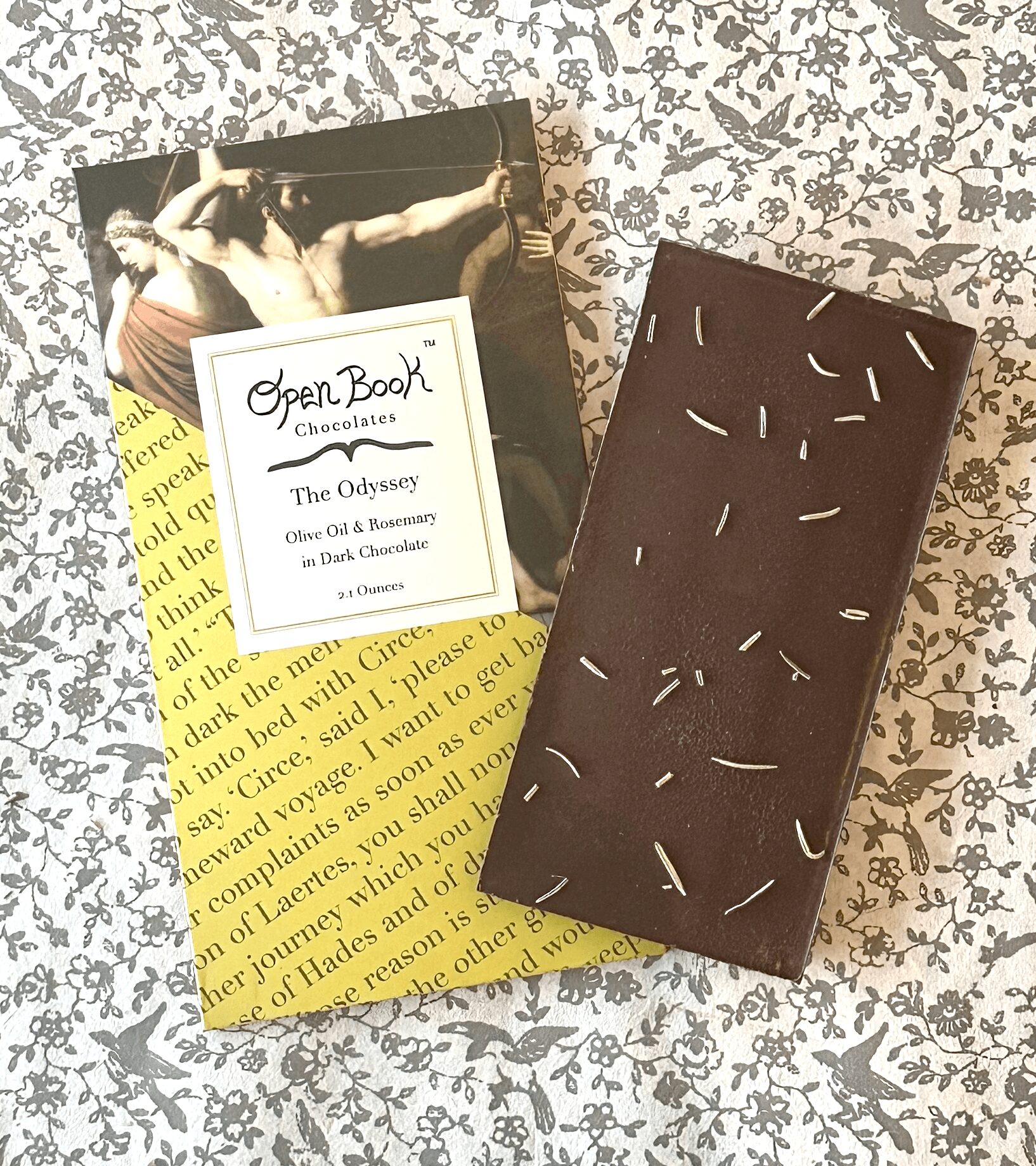 Chocolate bar with white sprinkles on a patterned surface, accompanied by a book and a yellow paper with text.