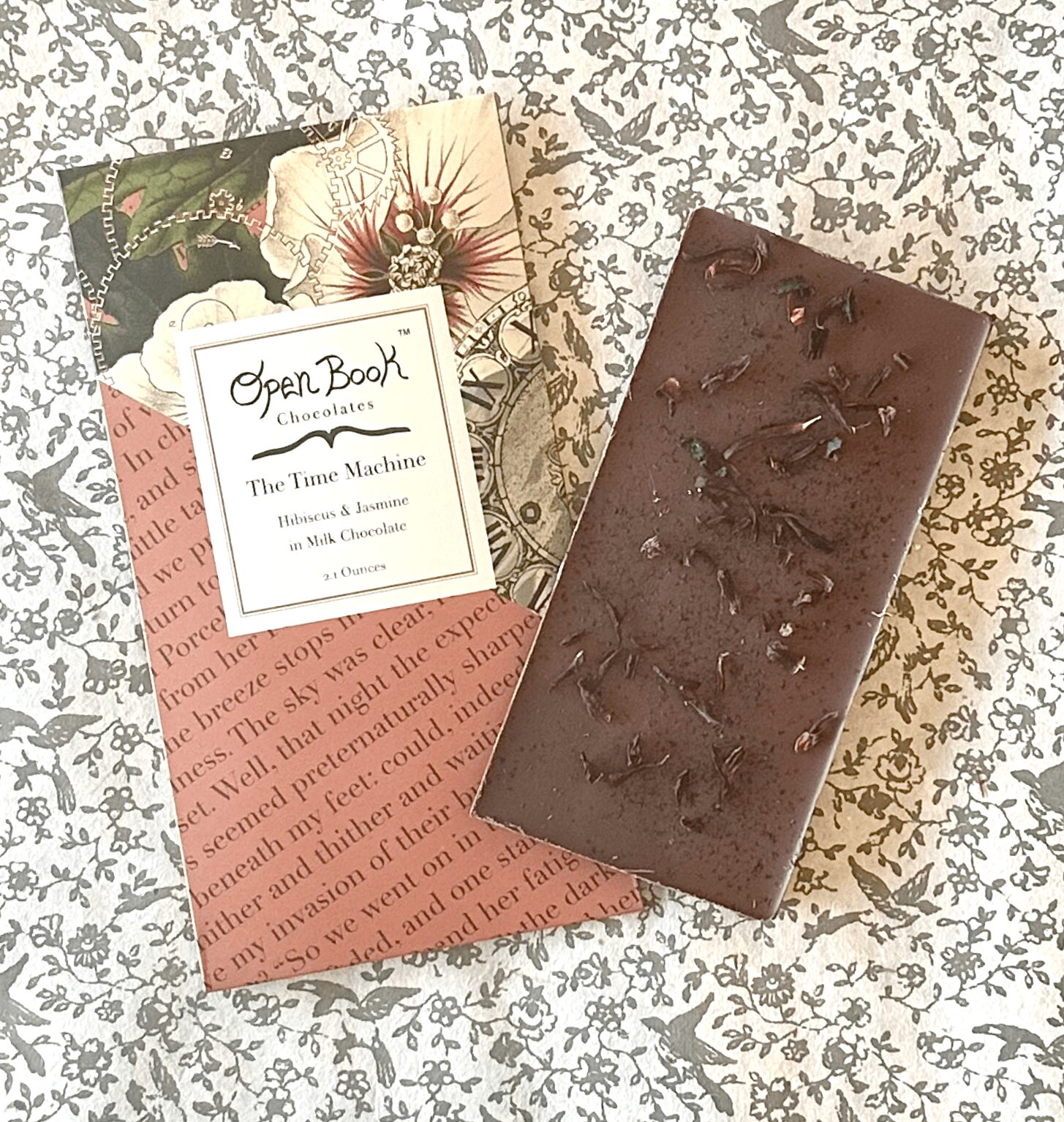 Chocolate bar on floral fabric with open book card and red paper, top side up, 20 words or fewer.