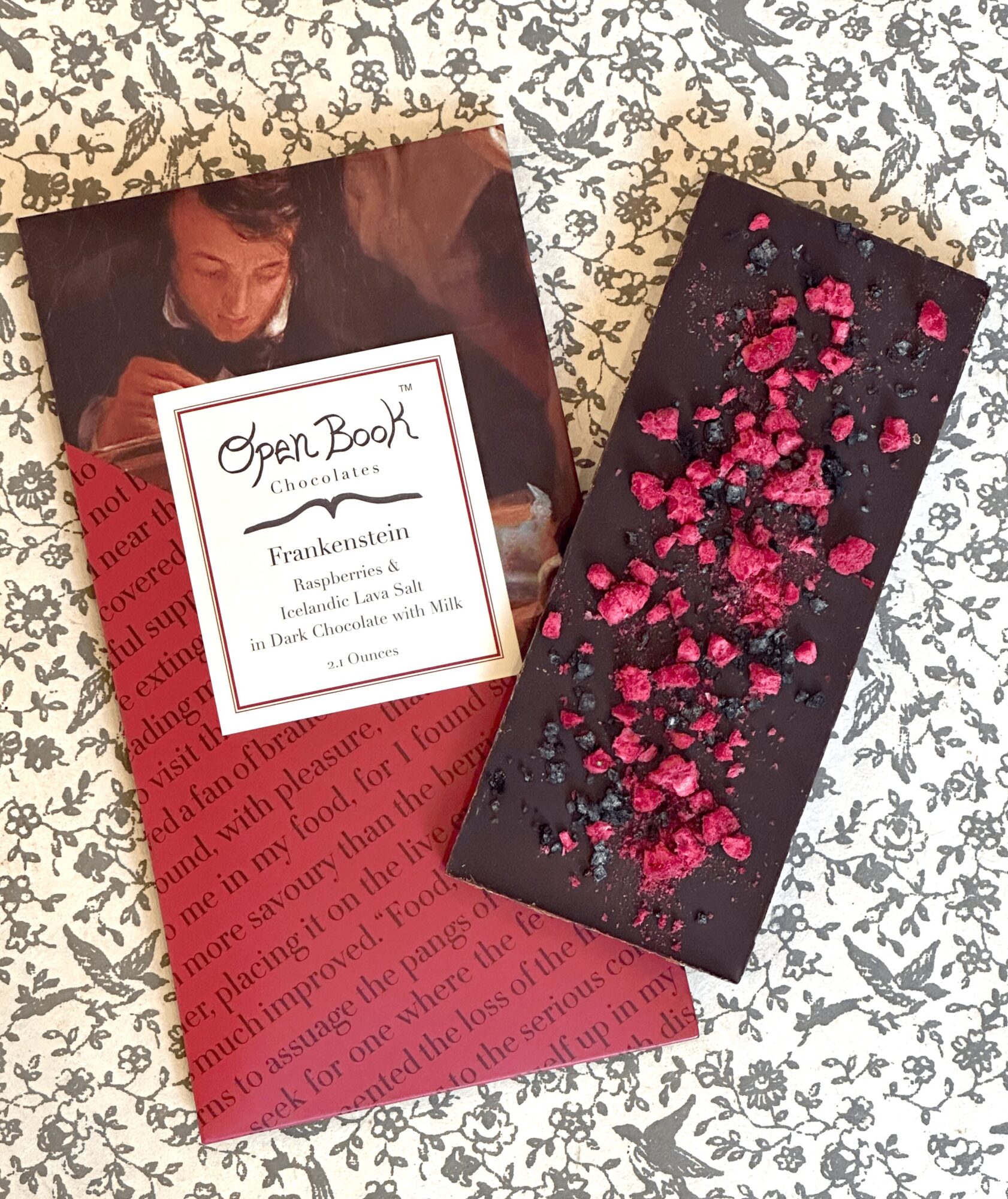 Chocolate bar with pink and red sprinkles on black surface, placed on patterned fabric background.