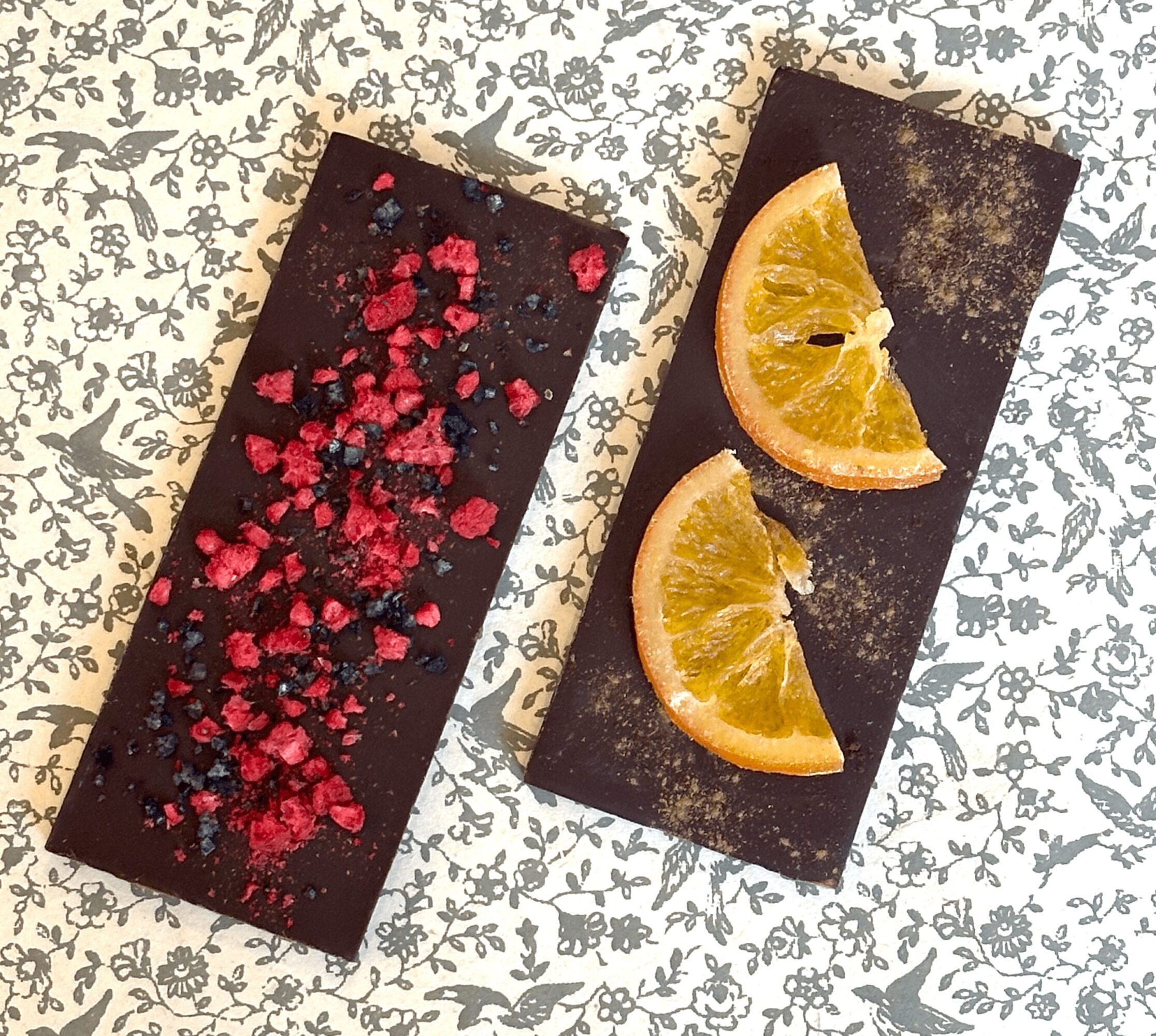 Two rectangular chocolate desserts on patterned paper, one topped with red and blue sprinkles, the other with lemon slices.